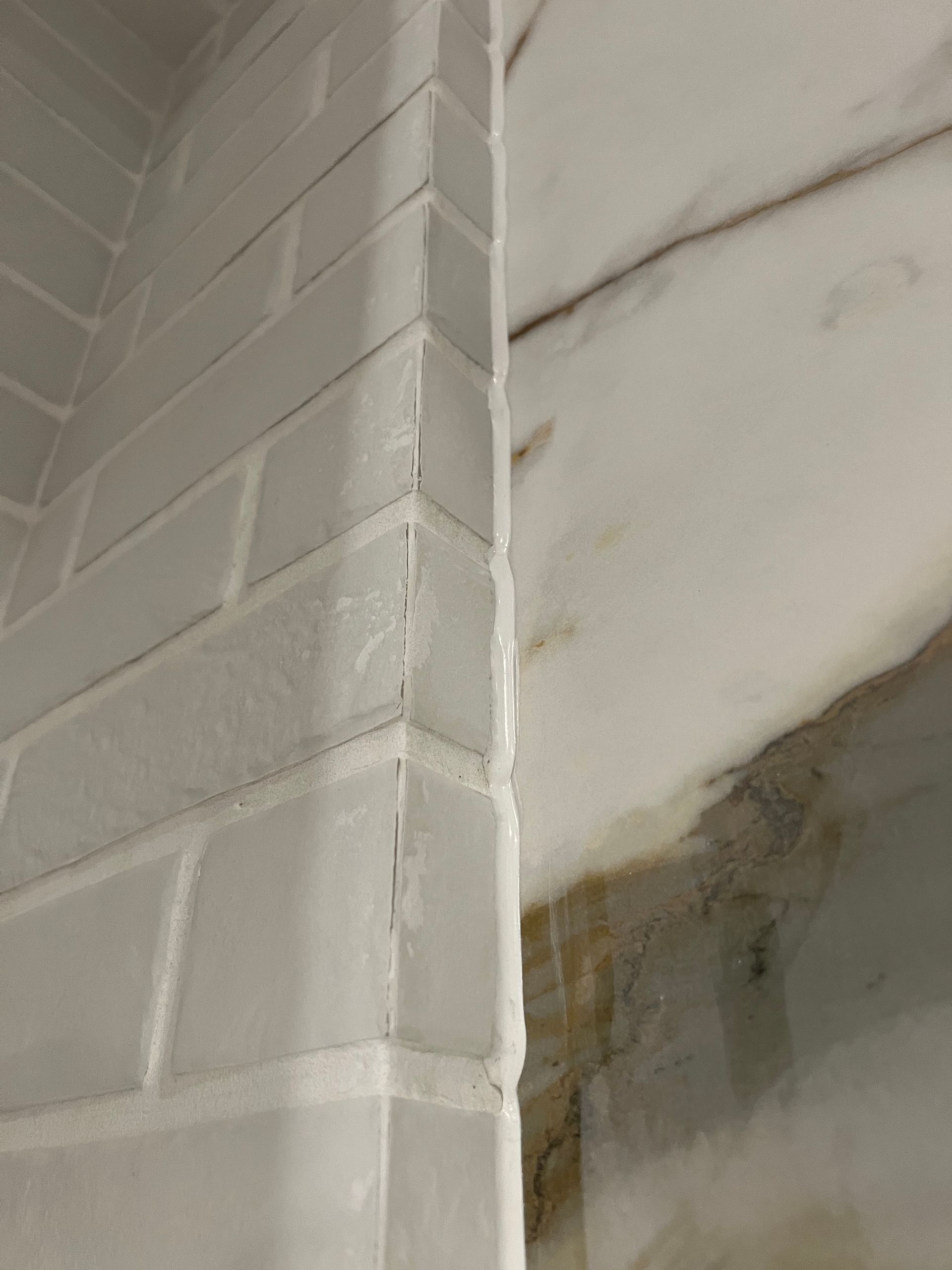 White brick-like tile wall corner; water stains on the ceiling.