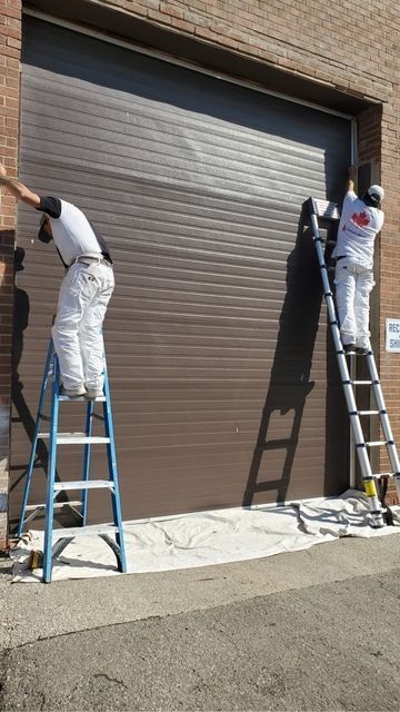 Two men on ladders are painting a garage door