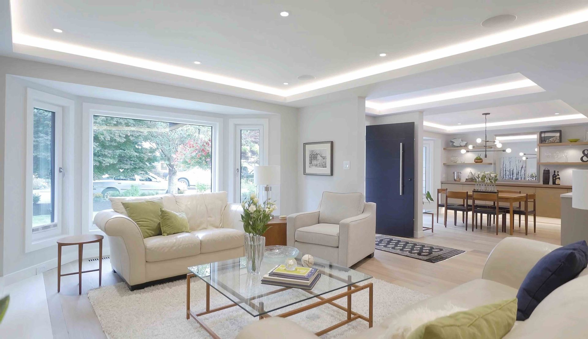 Bright open living room with beige sofas, glass coffee table, large windows, and a dining area beyond