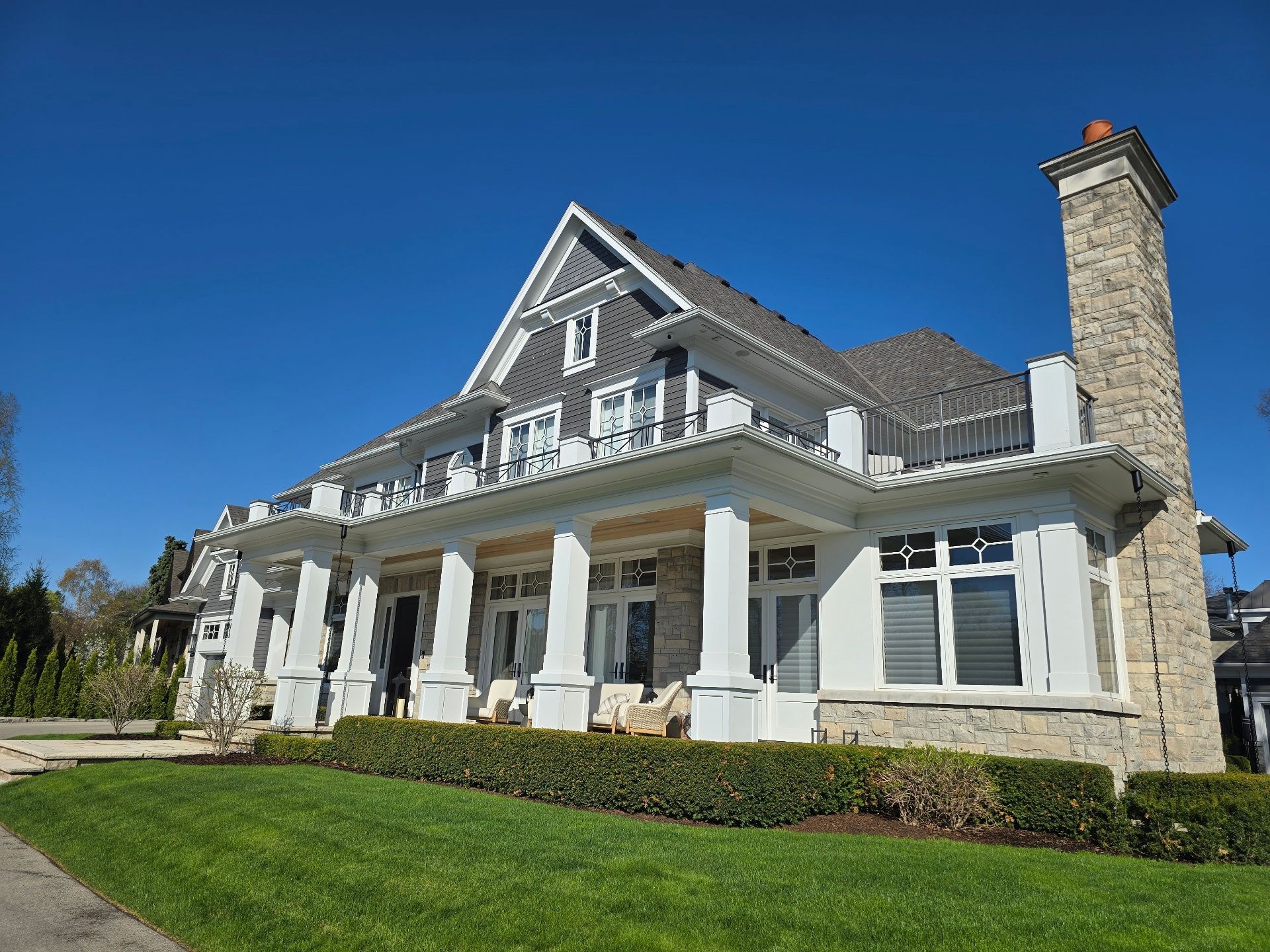 Large stone house with white porch columns, gray roof, and tall chimney under a clear blue sky