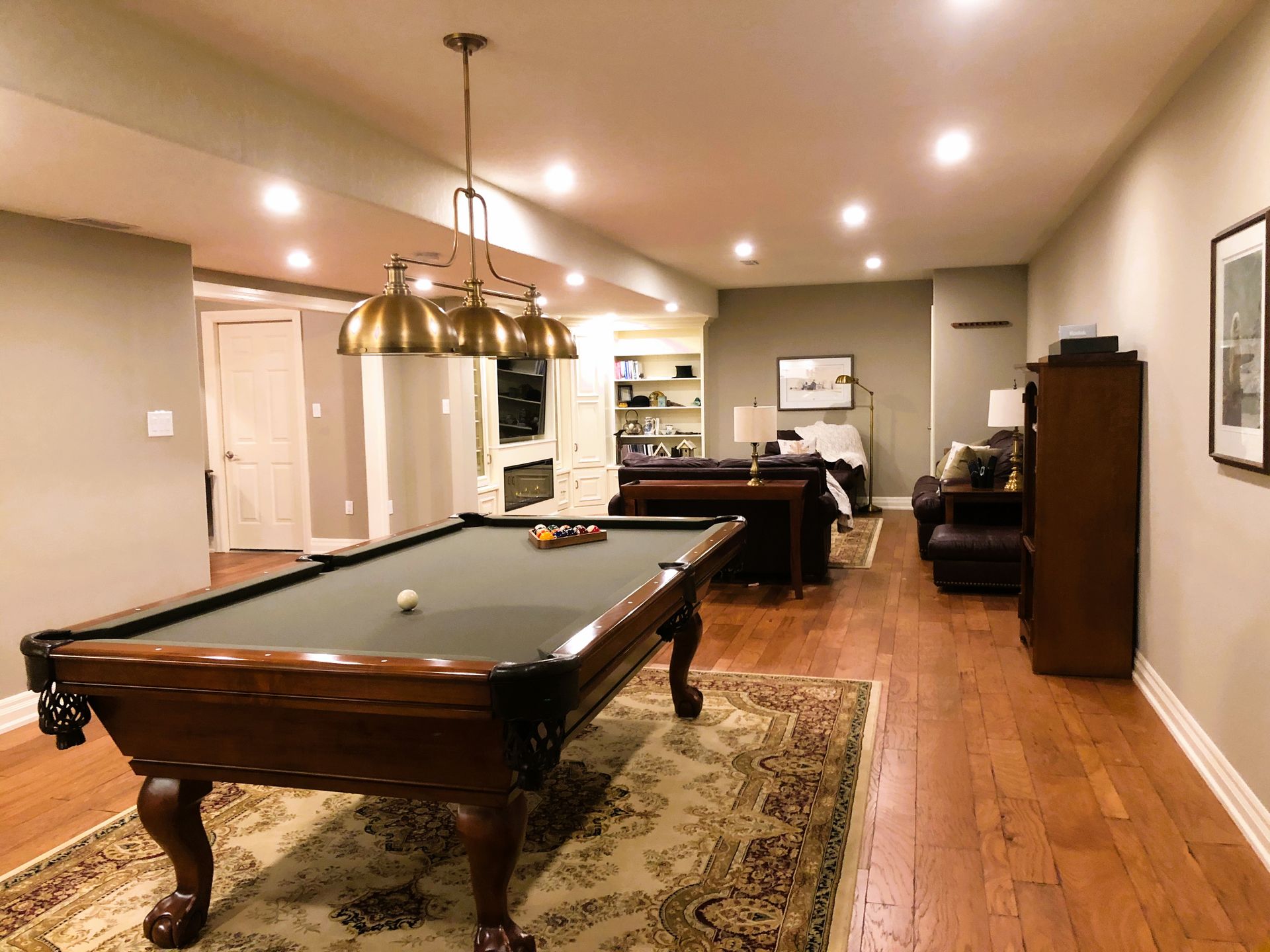 Pool table in finished basement with hardwood floors and seating area.