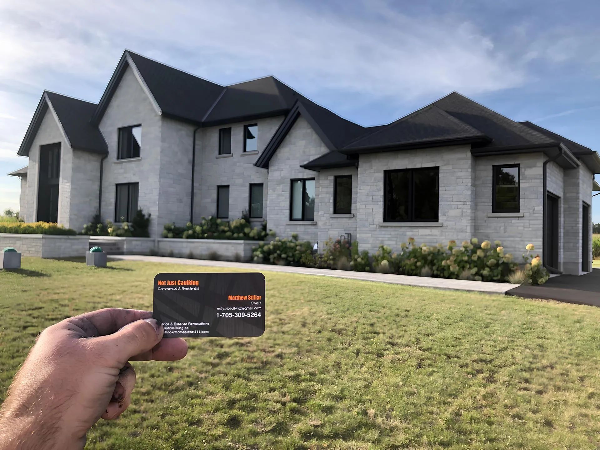 Hand holding a card in front of a large modern house with a landscaped yard