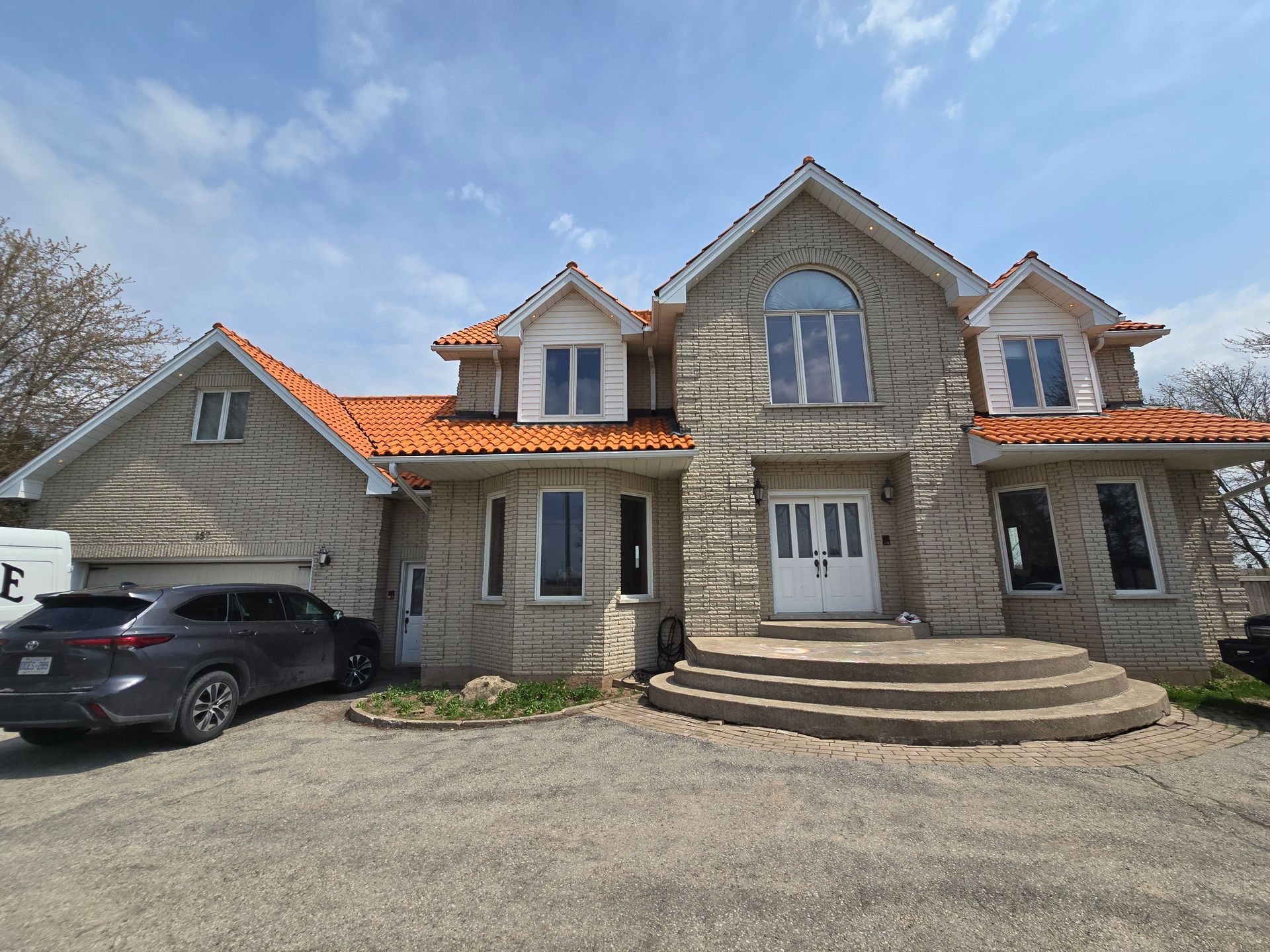 Large stone house with orange roof, arched windows, front steps, and a car parked in the driveway.