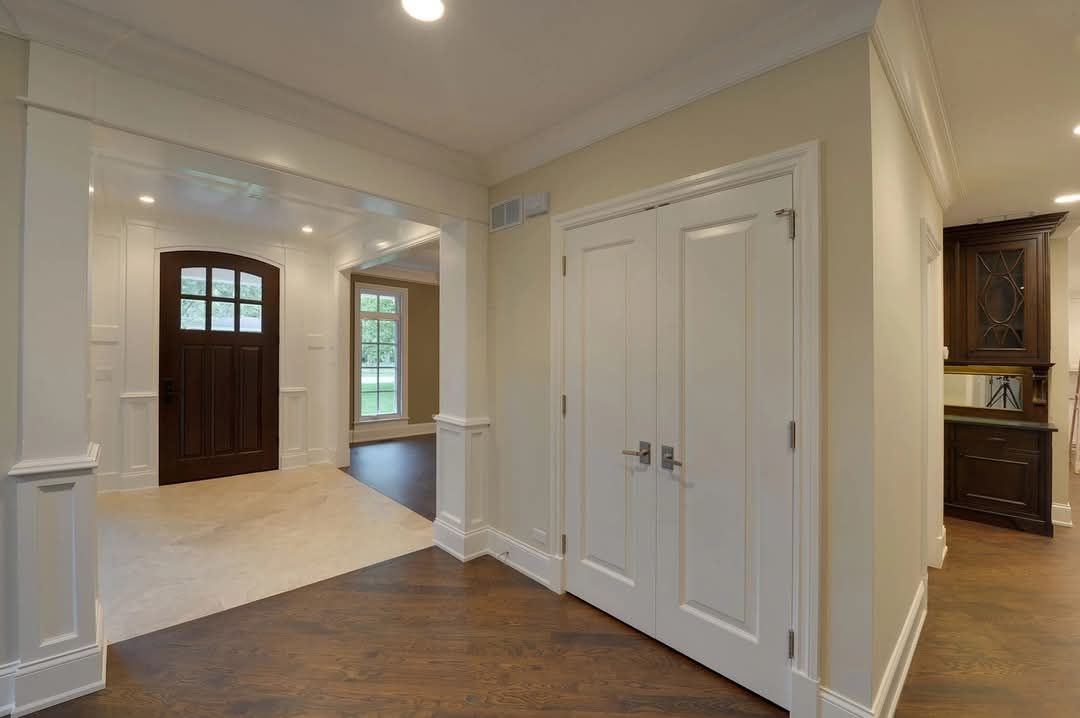 Bright foyer with dark wood floors, white trim, double closet doors, and an open view to a front entry.