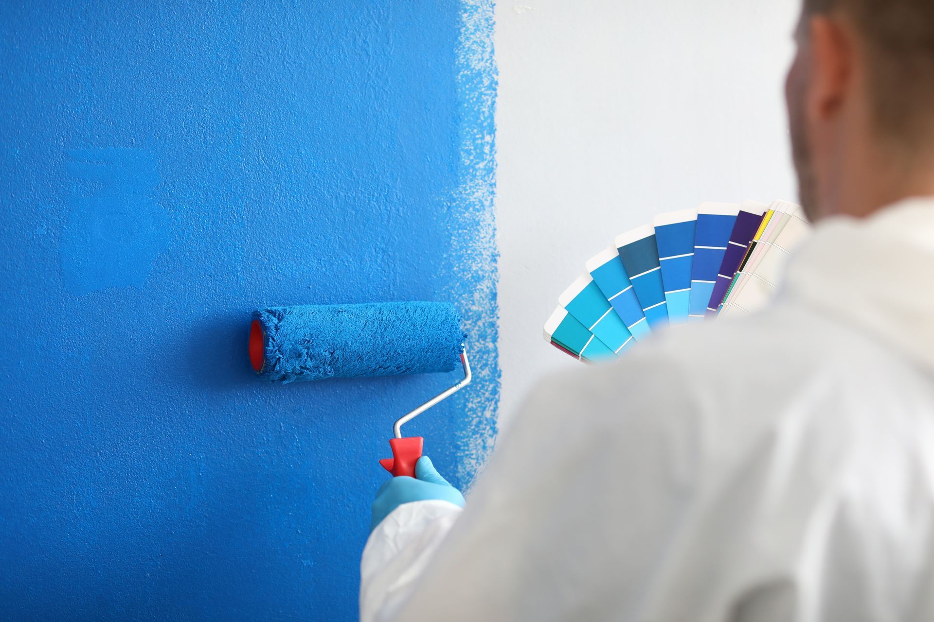 contractor paints a wall blue with a roller and holds a color palette in his other hand
