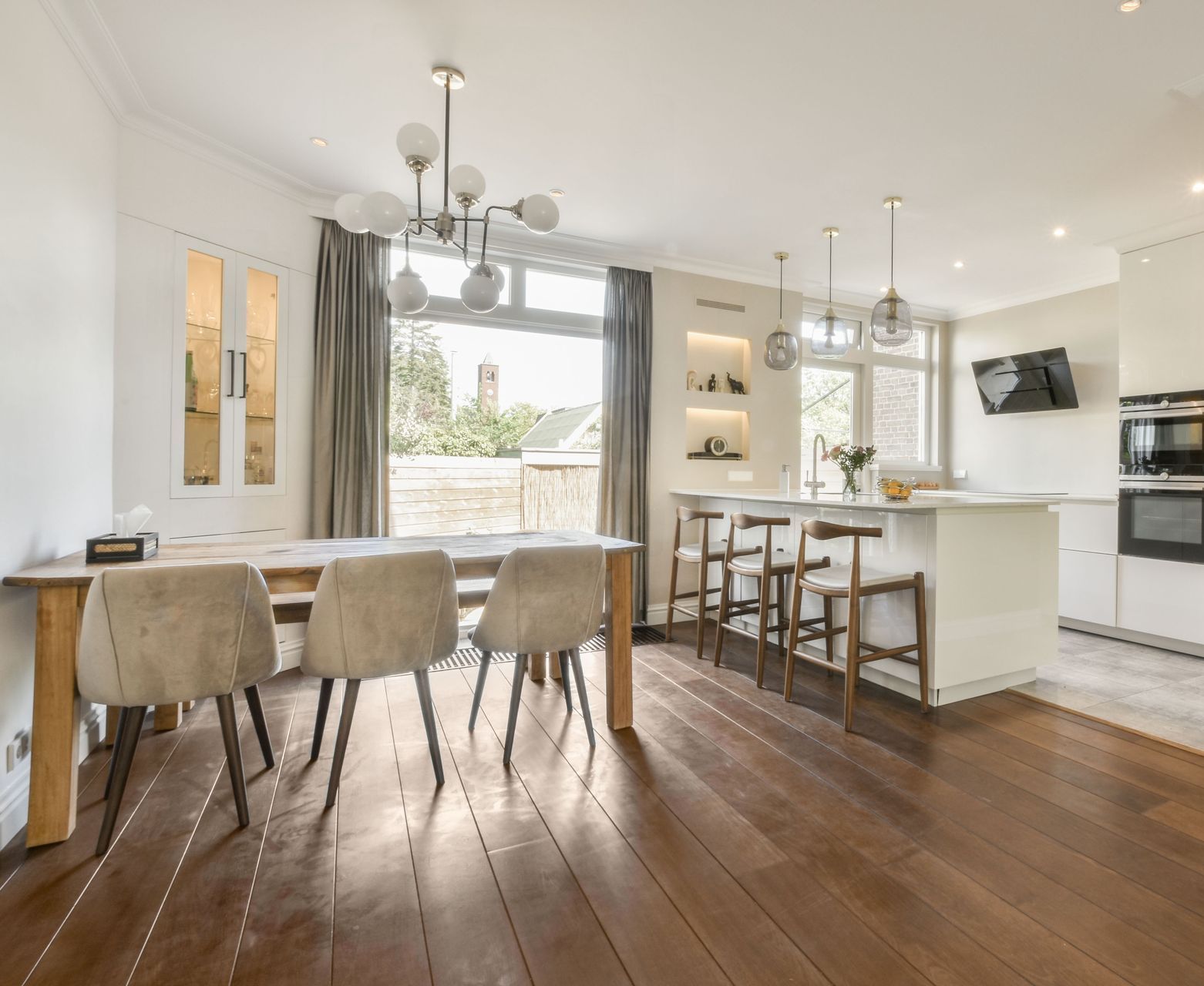 A dining room with a table and chairs and a kitchen in the background.