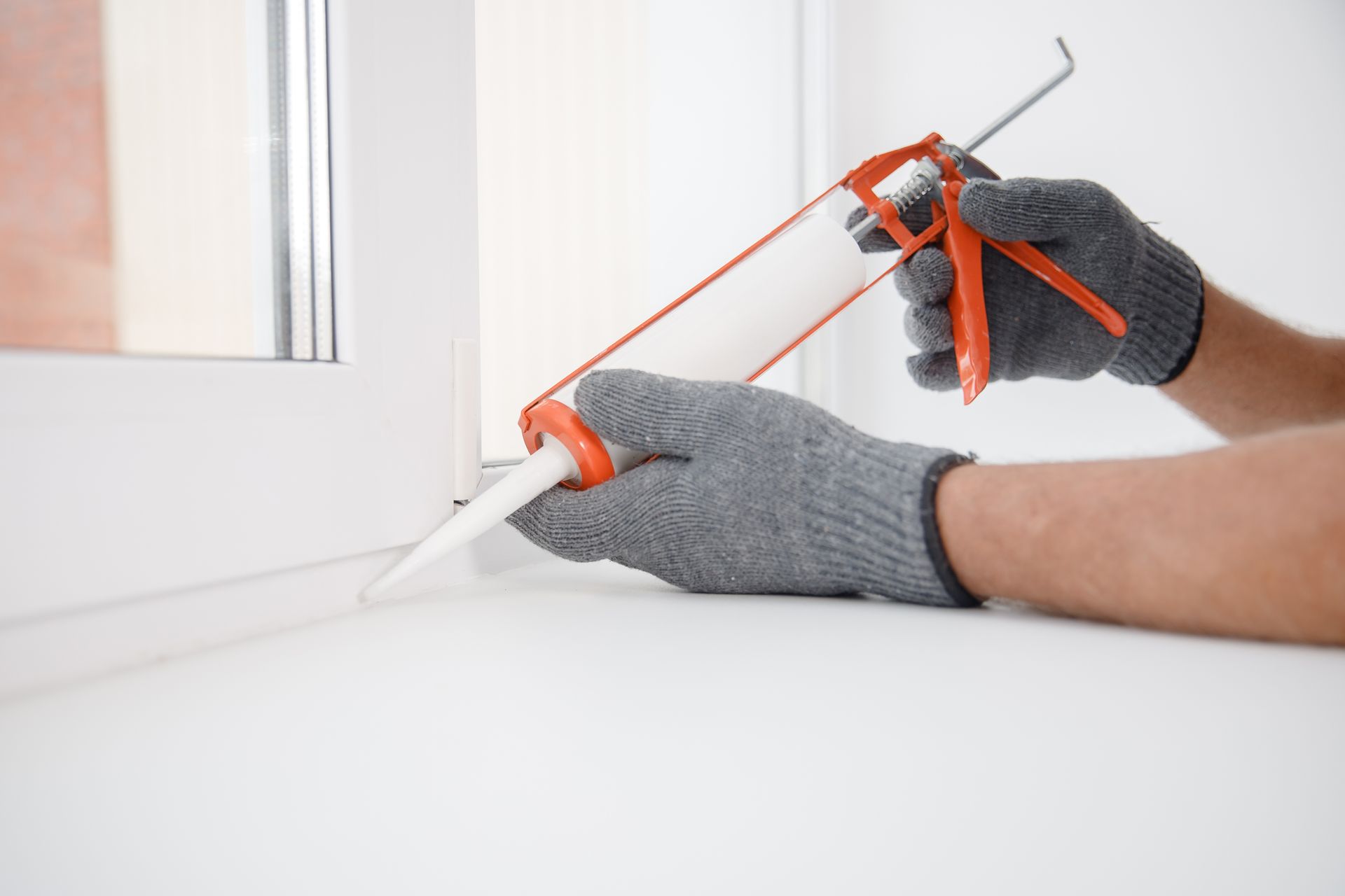 A person is applying sealant to a window sill.