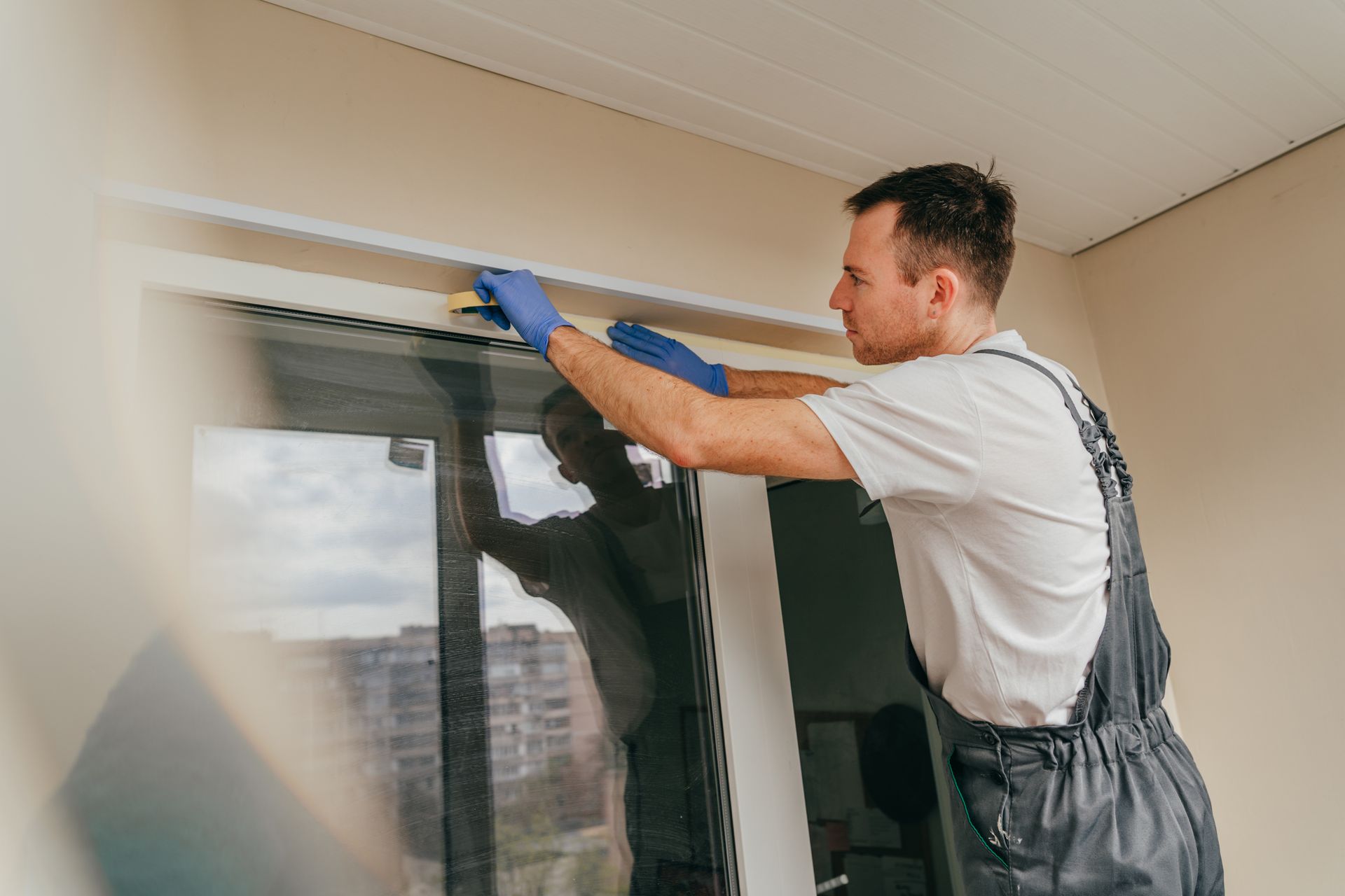 Man in blue gloves installing a white trim above a window.