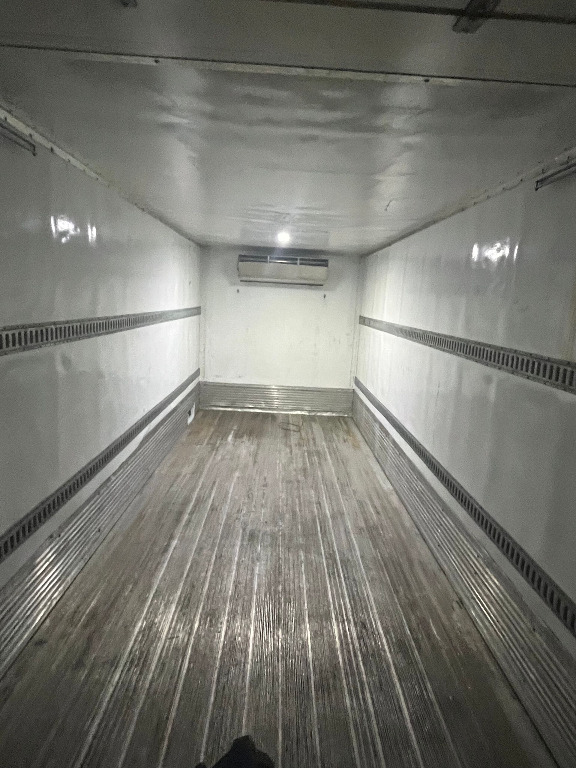 Empty refrigerated truck interior, white walls, grooved floor, ceiling-mounted AC unit, tie-down rails.