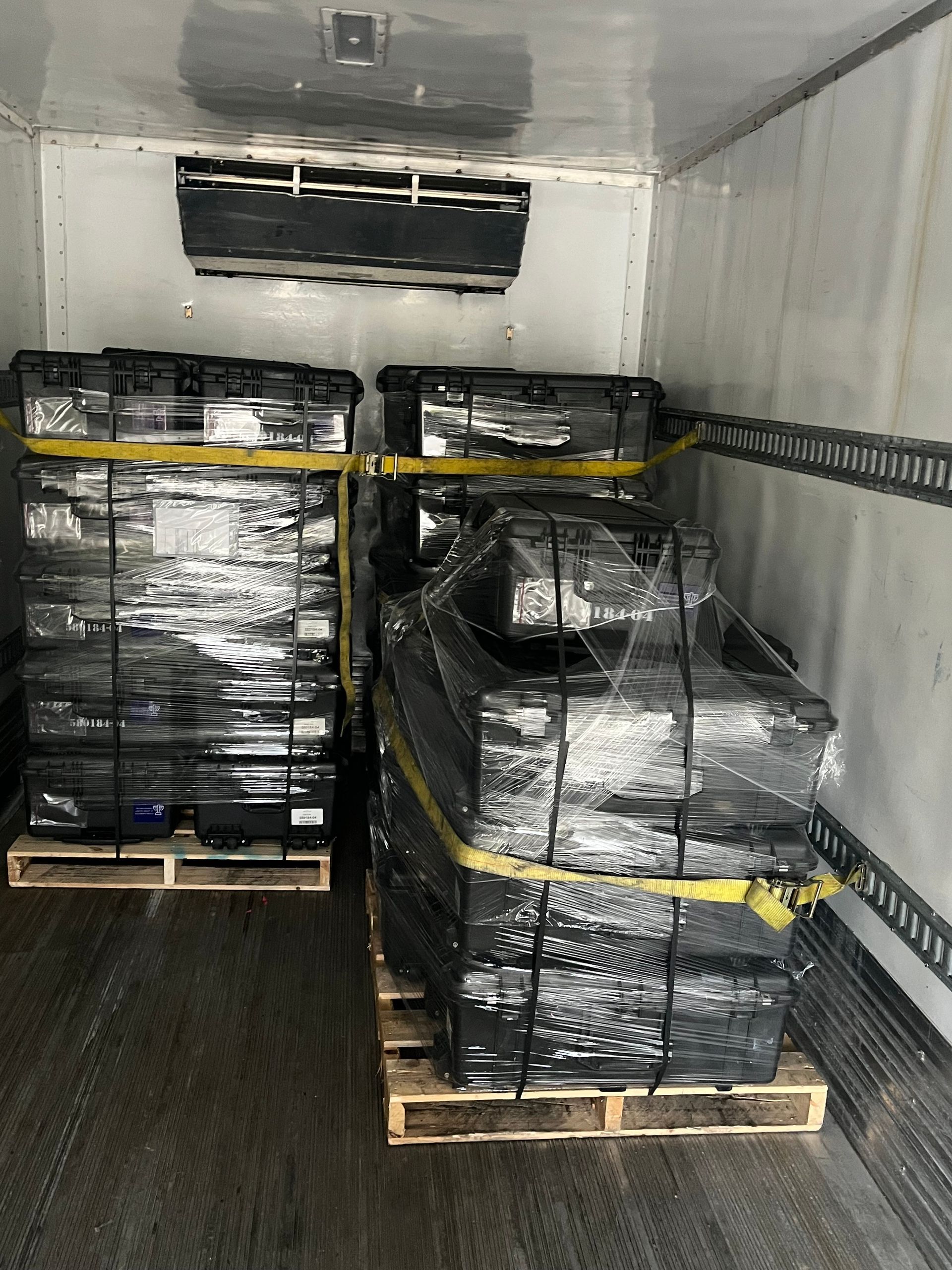 Pallets of black-wrapped items secured with yellow straps inside a refrigerated truck.
