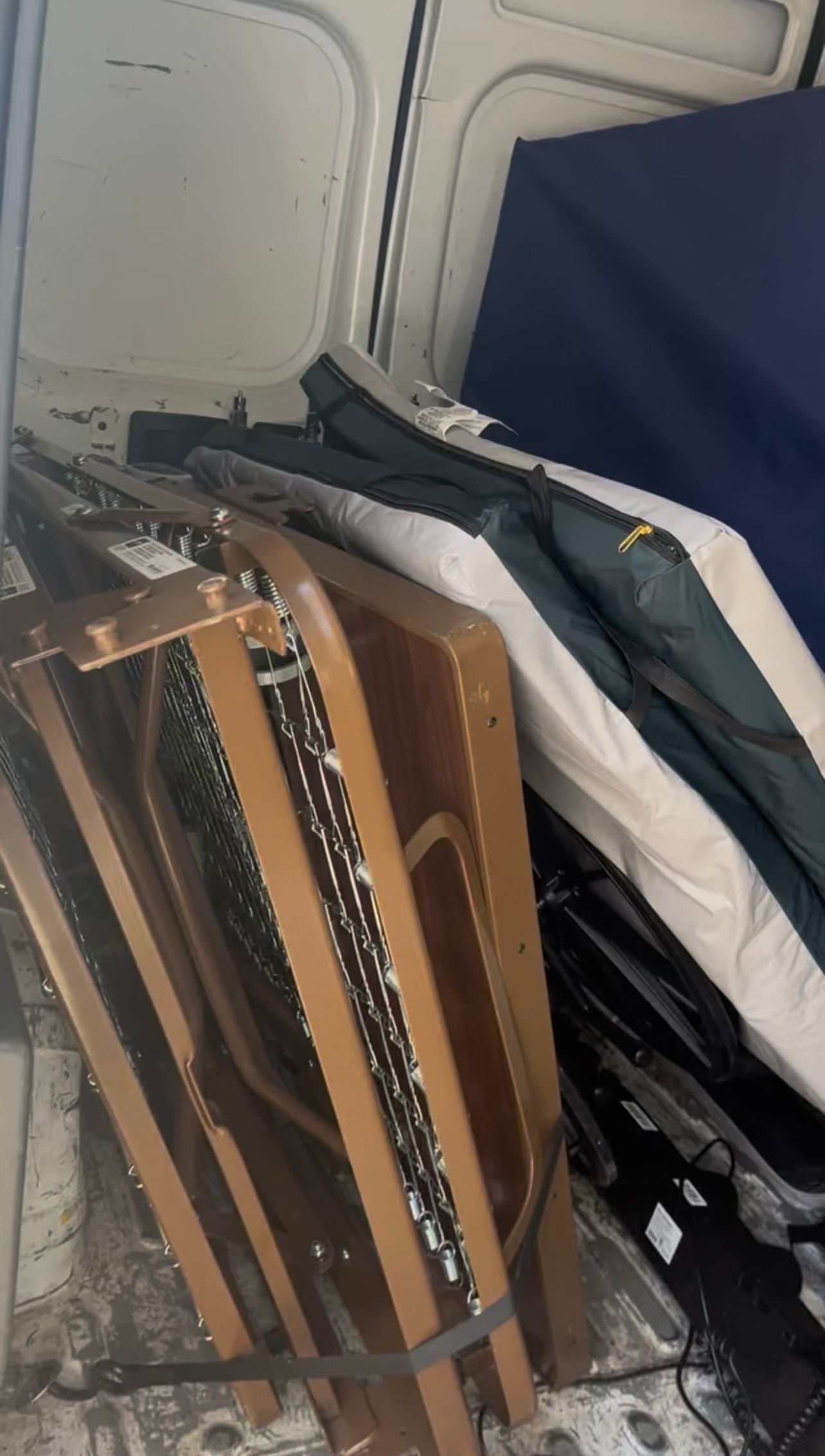 Inside a white van, stacked wooden folding chairs with other items, including bedding.