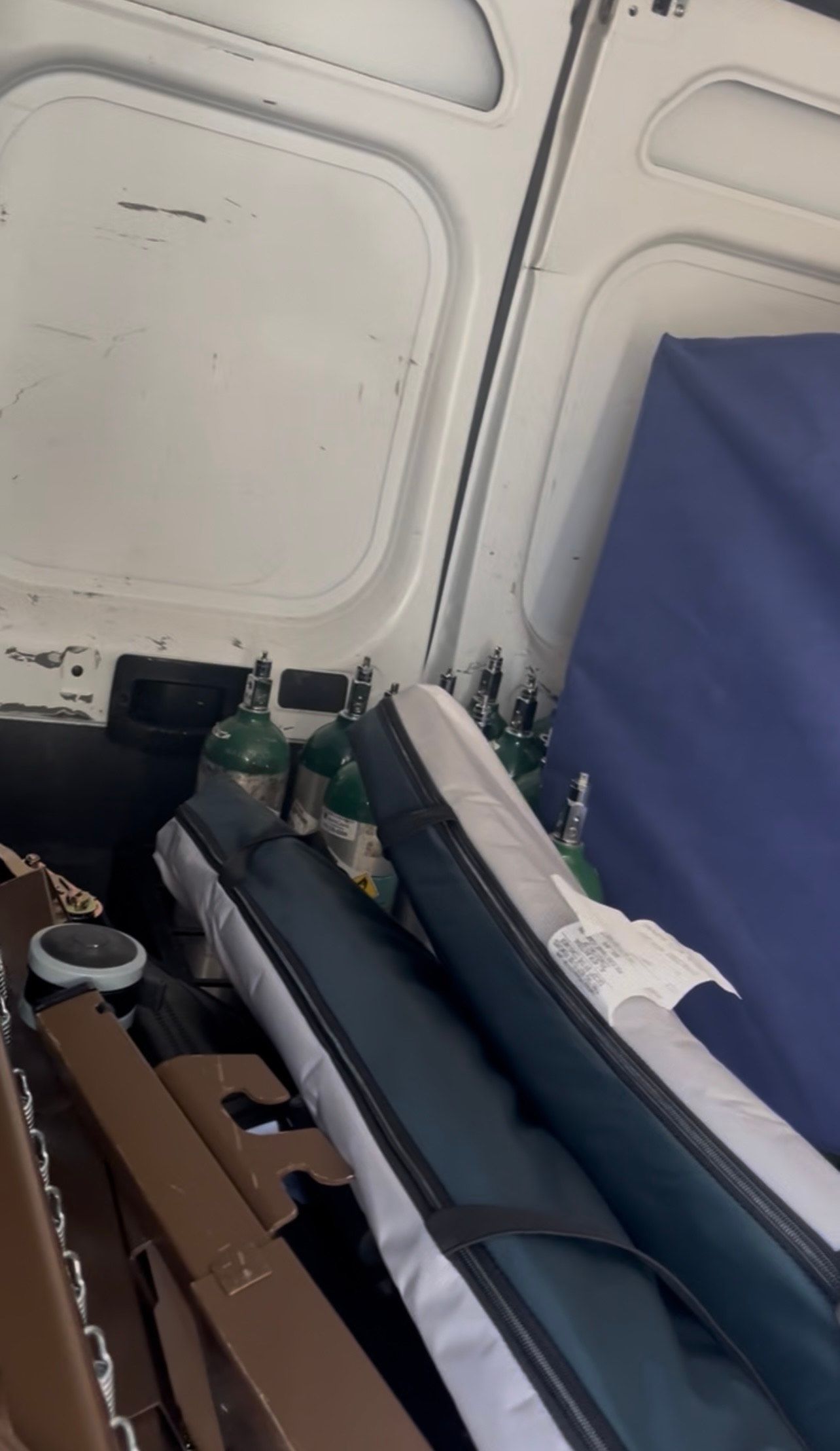 Inside of a white van, oxygen tanks and two long, narrow cases are visible.
