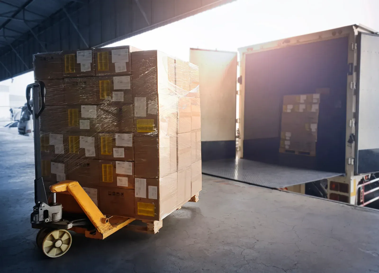 Pallet of boxes on a hand truck being loaded into a truck at a loading dock.