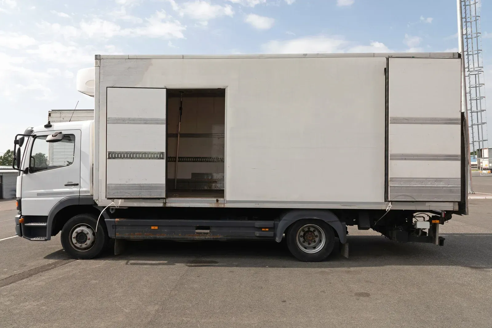 Semi-truck driving on a road at dusk. Red taillights and a white trailer against a blue sky.