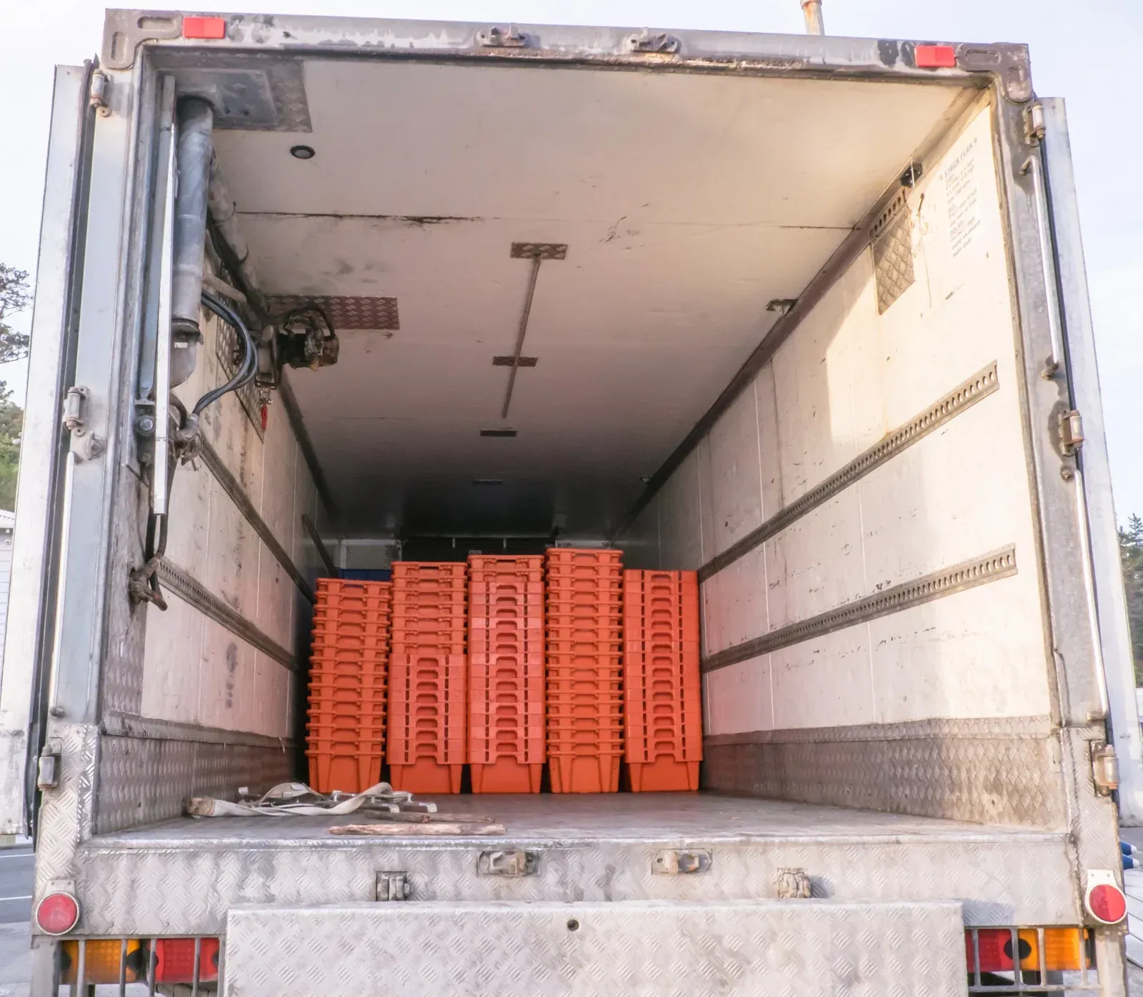 Open rear of a refrigerated truck, revealing orange plastic crates inside.