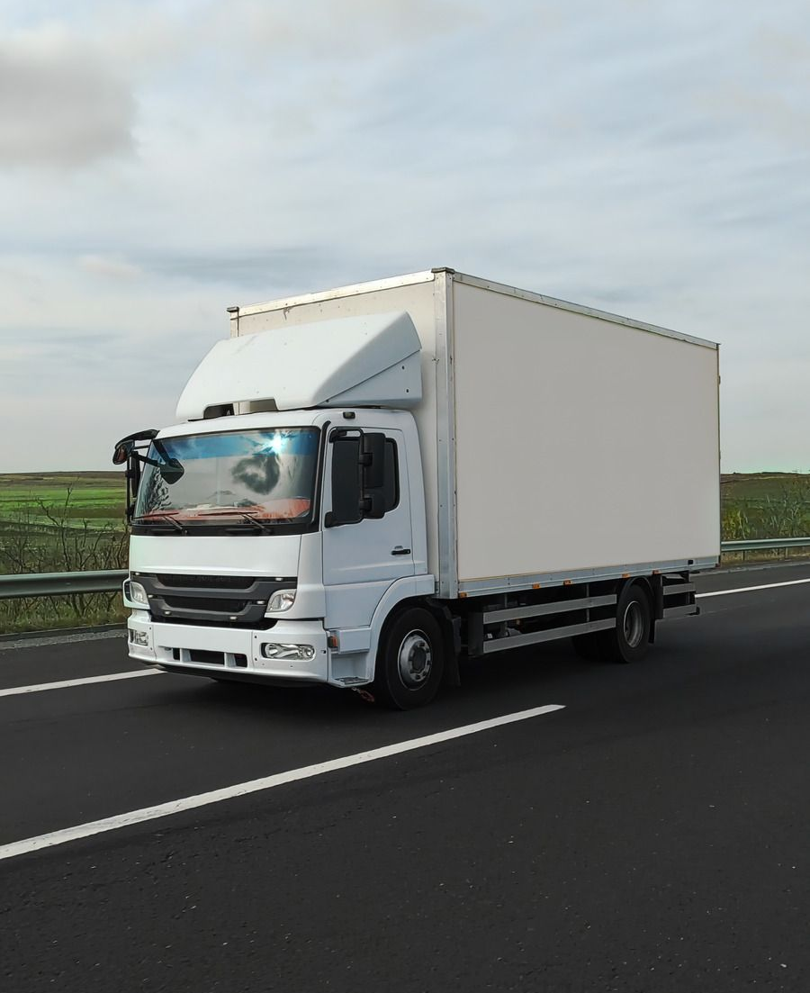 White semi-truck driving on a highway with a blue sky and clouds.