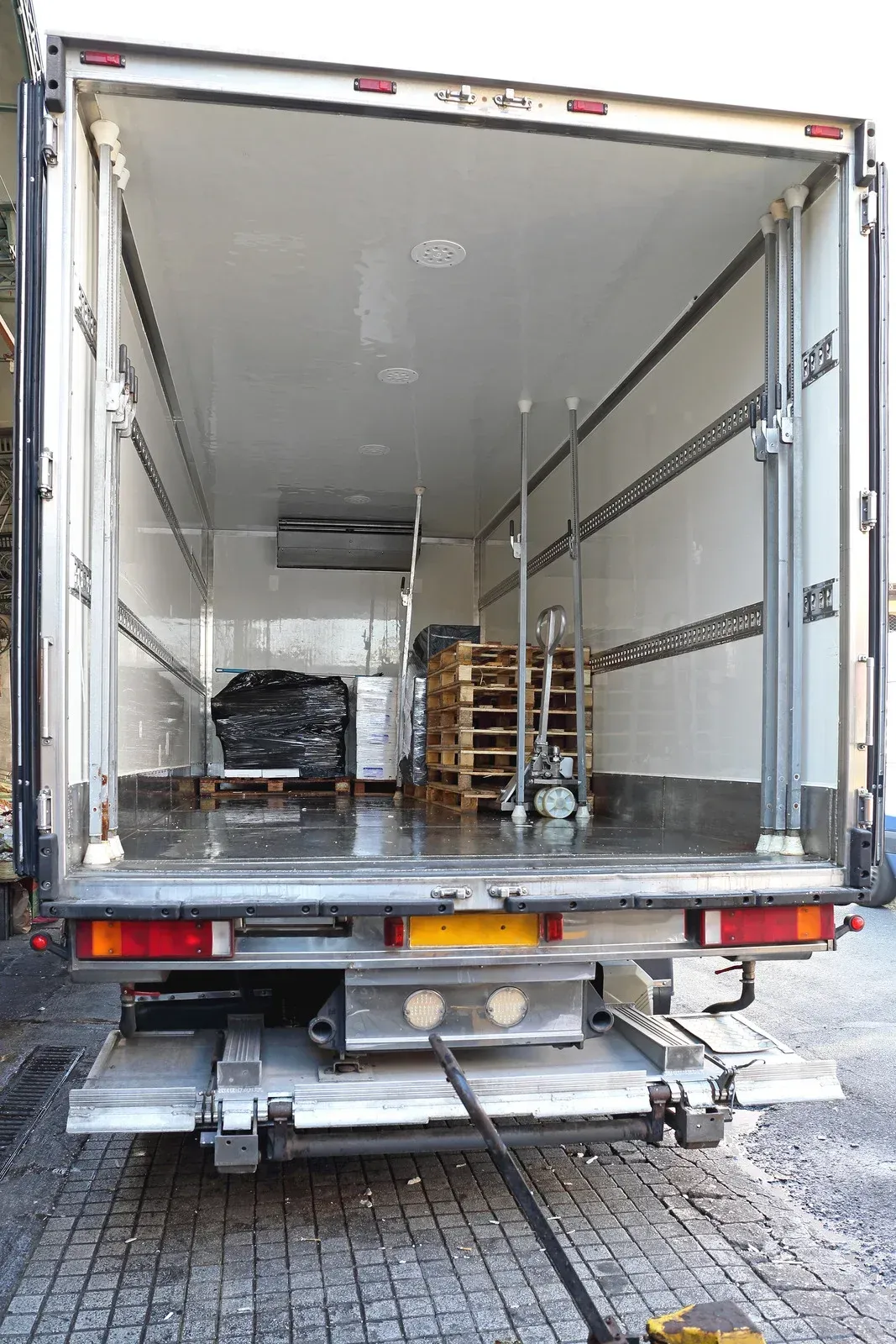 Open back of a refrigerated truck with pallets, goods, and lift gate.