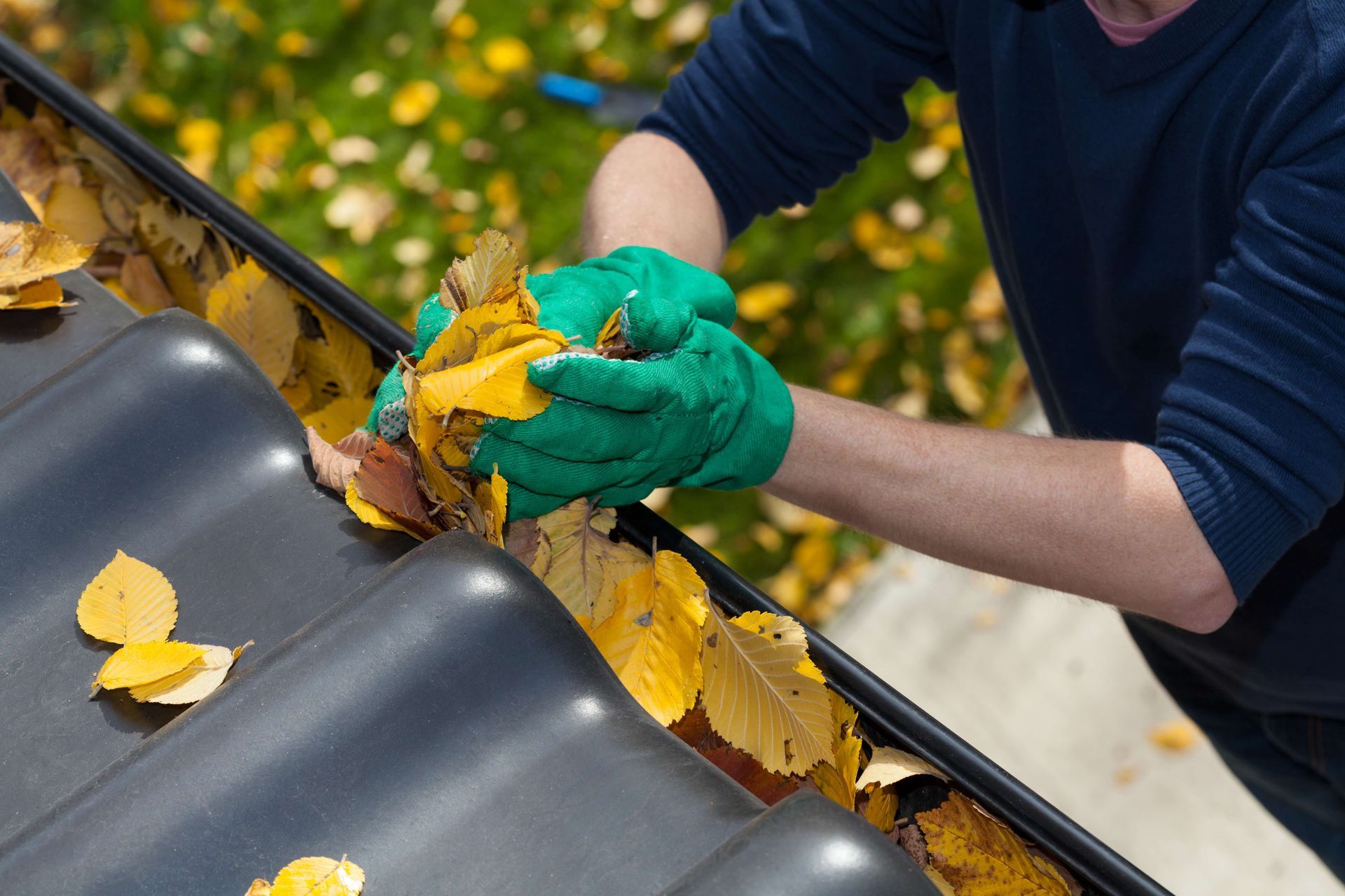 a man wearing green gloves is cleaning a gutter with leaves