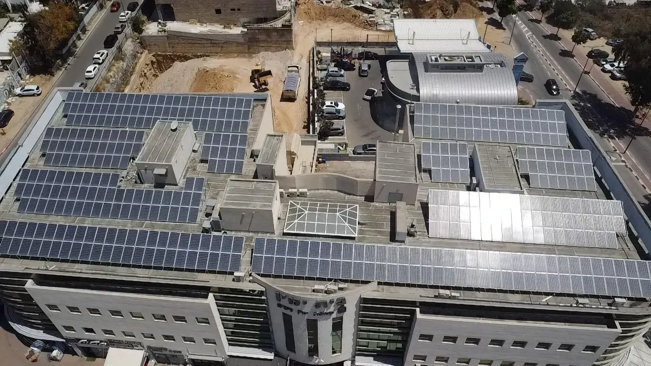 נוף מגג בניין עם פאנלים סולאריים, חניון ואתר בנייה.