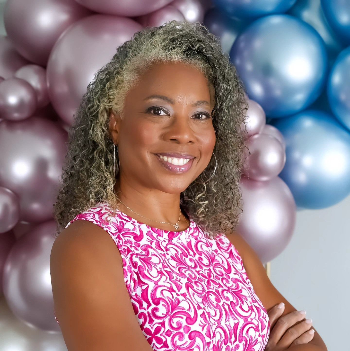 A woman in a pink dress is smiling in front of balloons.