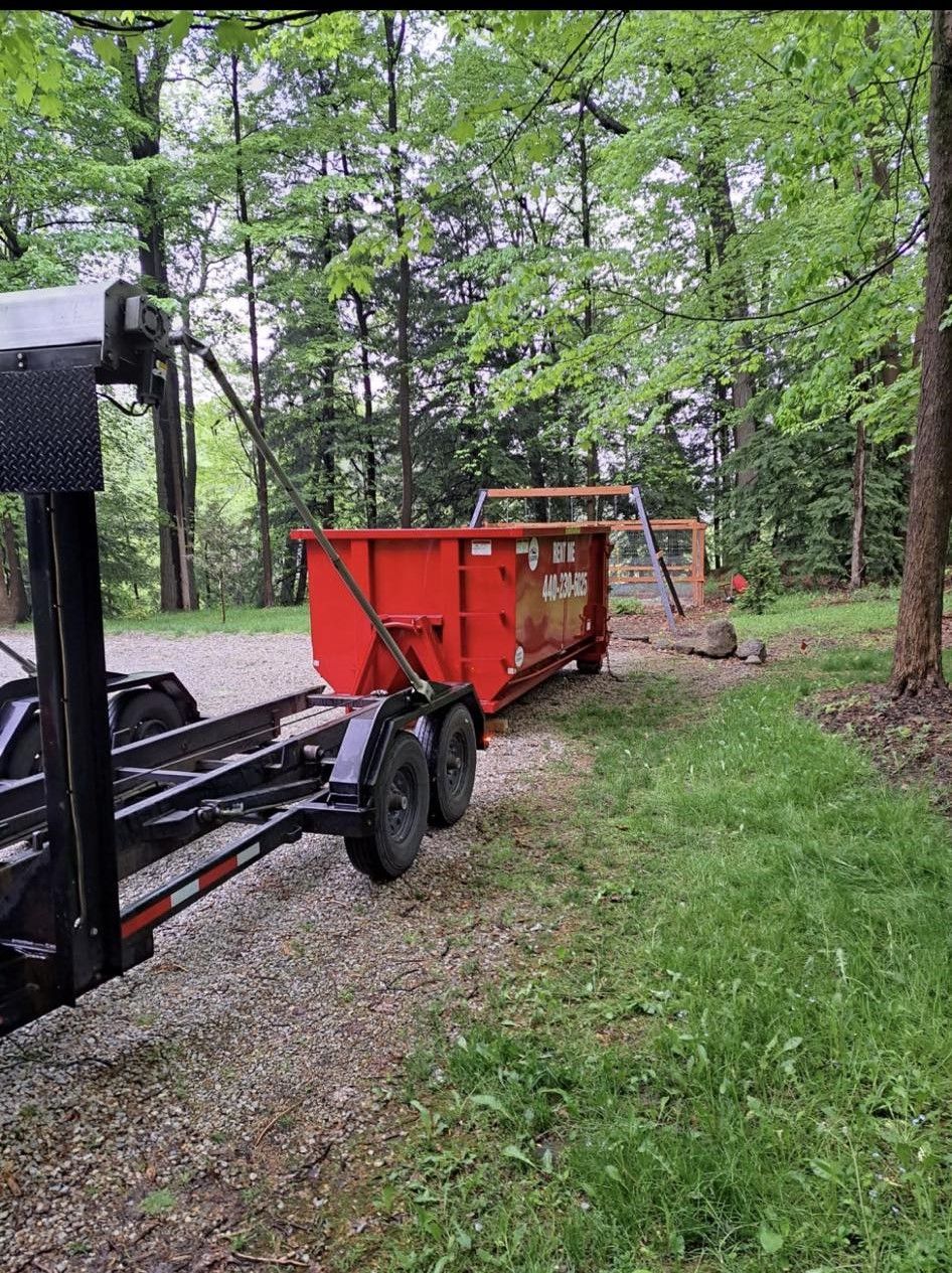 a dumpster is being pulled by a trailer in the woods .