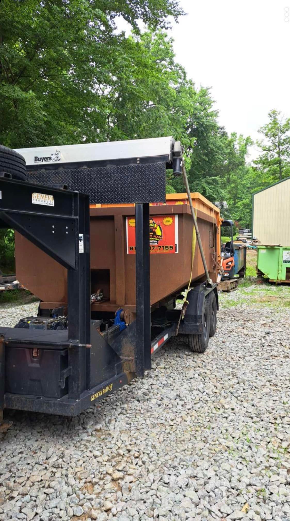 a dumpster is sitting on top of a trailer in a gravel lot .