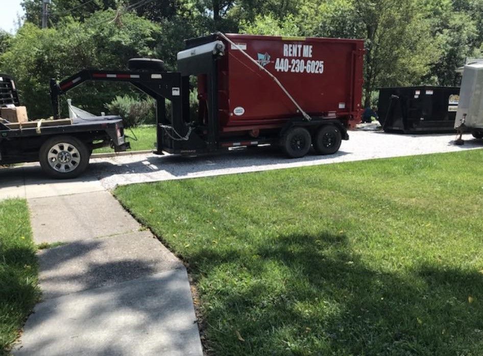 a red dumpster is parked in a driveway next to a truck .