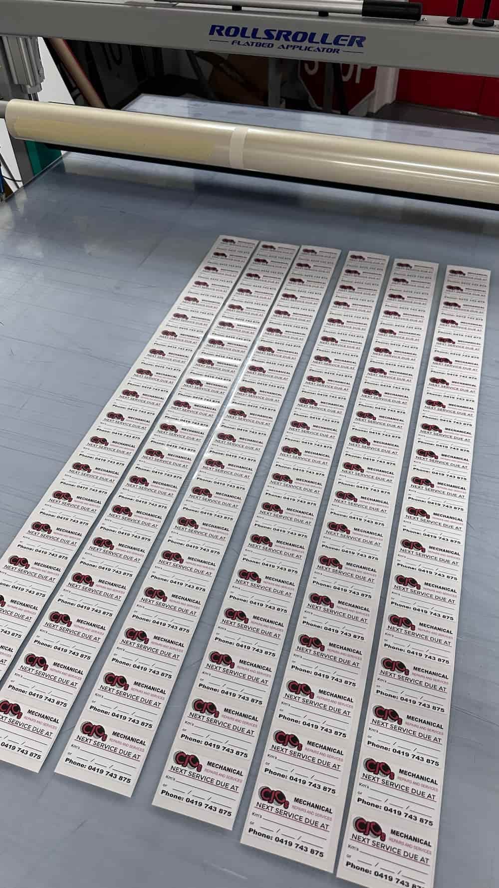 A Bunch of Stickers Are Sitting on a Table Next to a Machine — Global Signage In Ingham, QLD