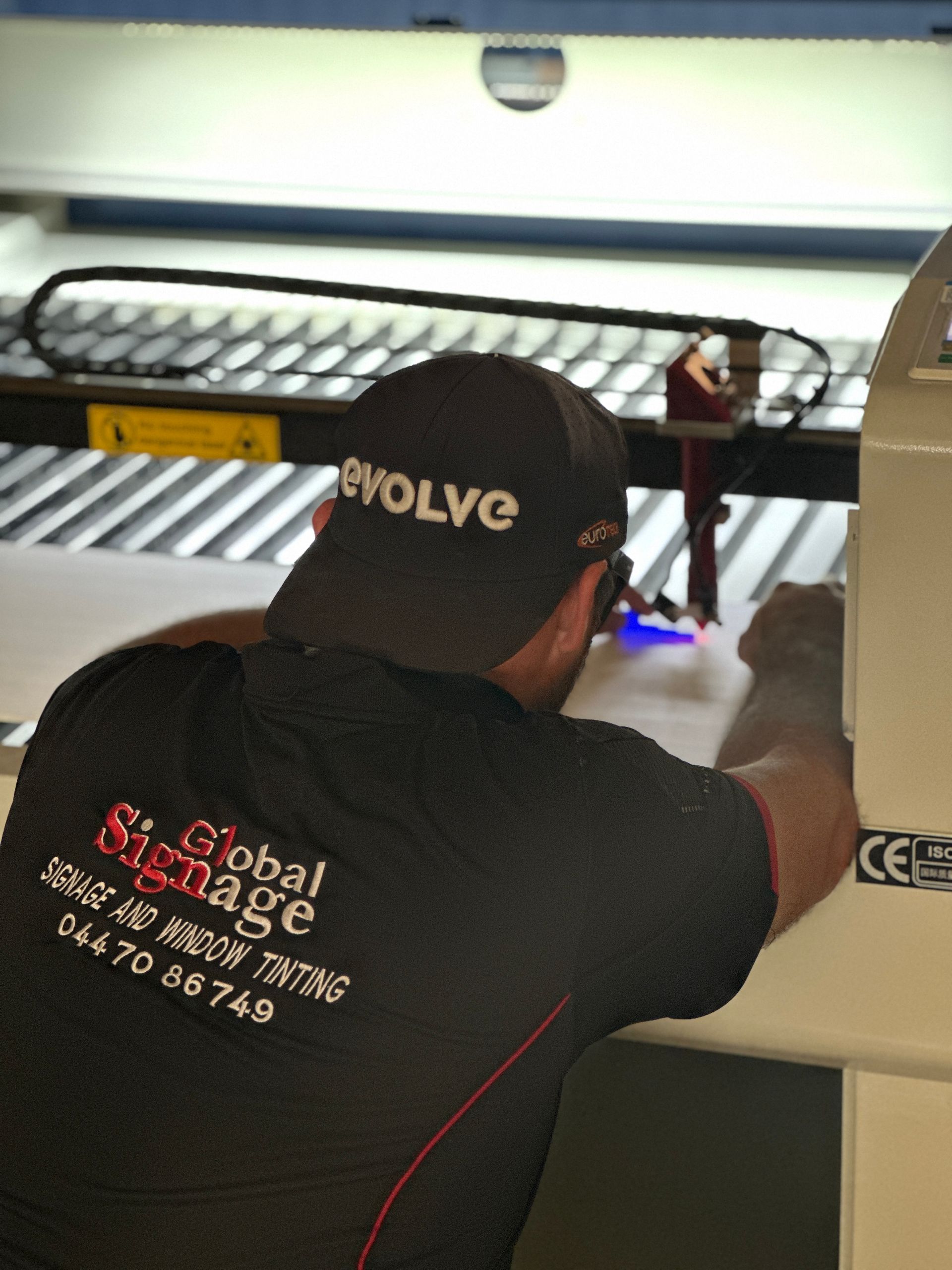 A man wearing a global signage hat is working on a machine — Global Signage In Ingham, QLD