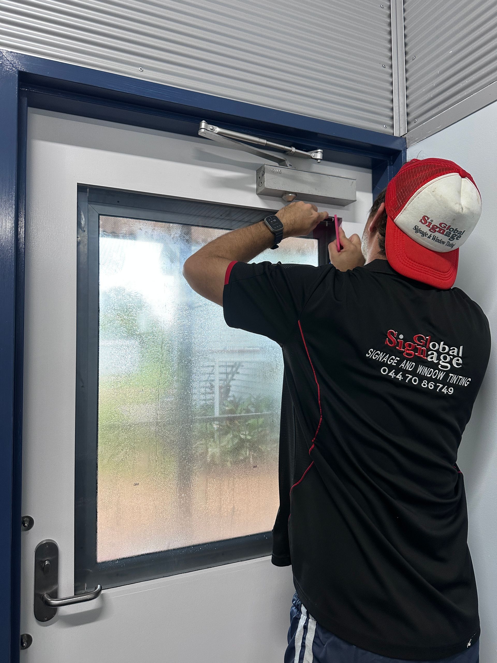 A man wearing a red hat is standing in front of a window — Global Signage In Ingham, QLD