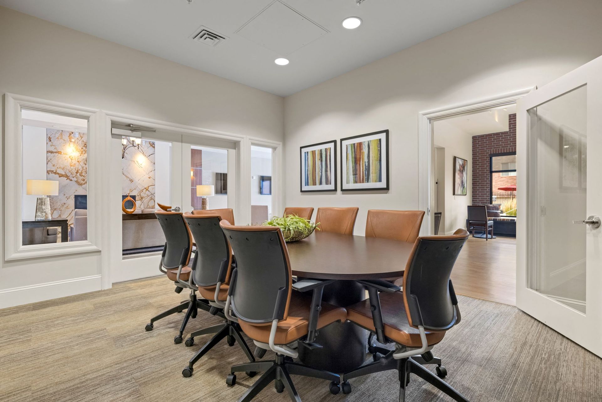 Meeting room with a round wooden table and tan leather chairs in a modern community space.