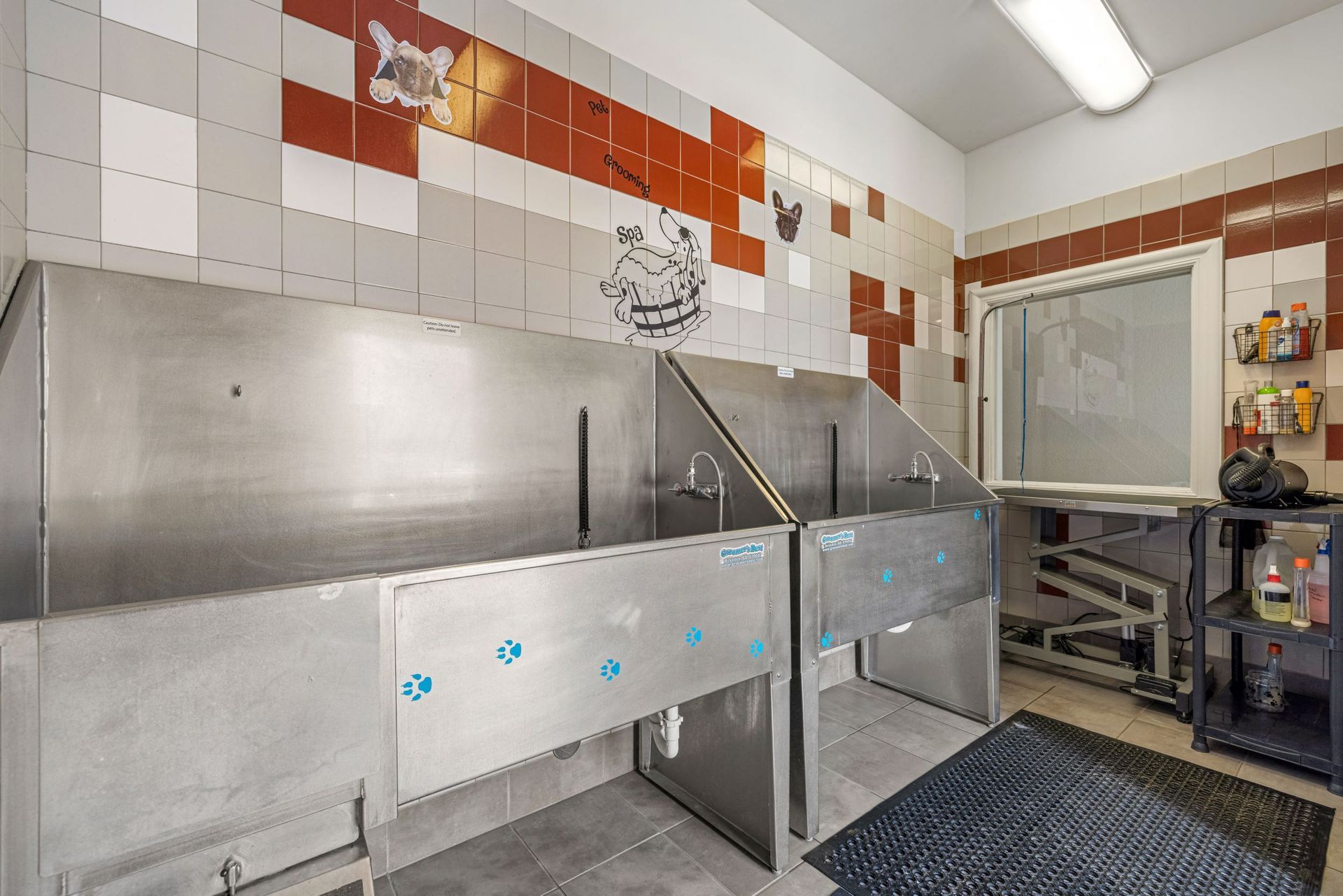 Pet washing station with stainless steel troughs and tiled walls.