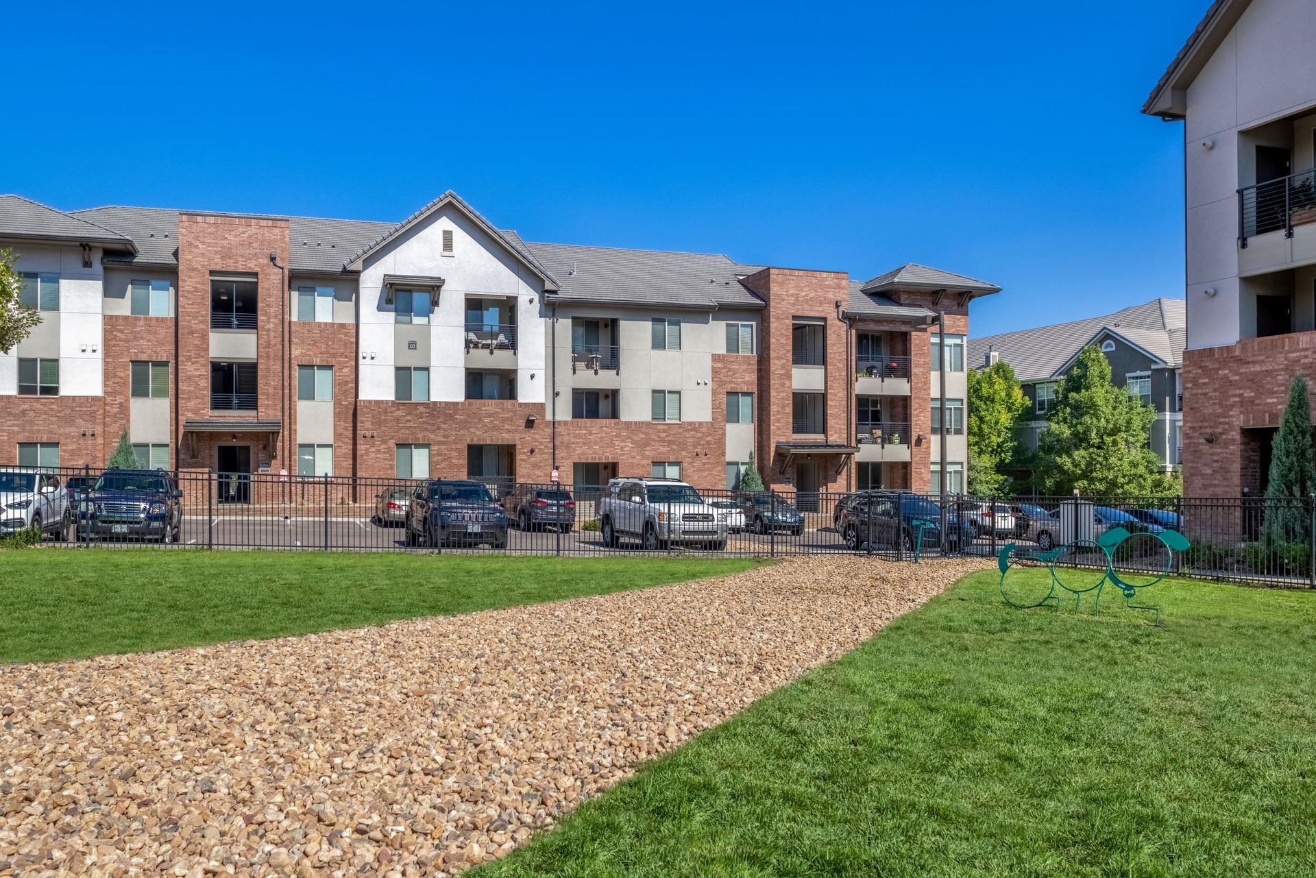 Exterior view of a multi-building apartment community with parking and green lawn.