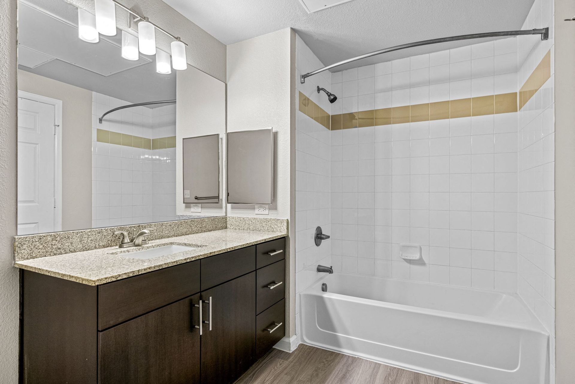 Bathroom with granite vanity, large mirror, and white tiled tub/shower in an apartment.