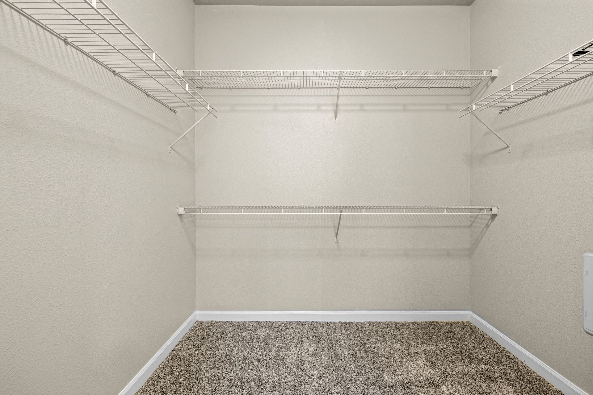 Empty walk-in closet with white wire shelves along beige walls.