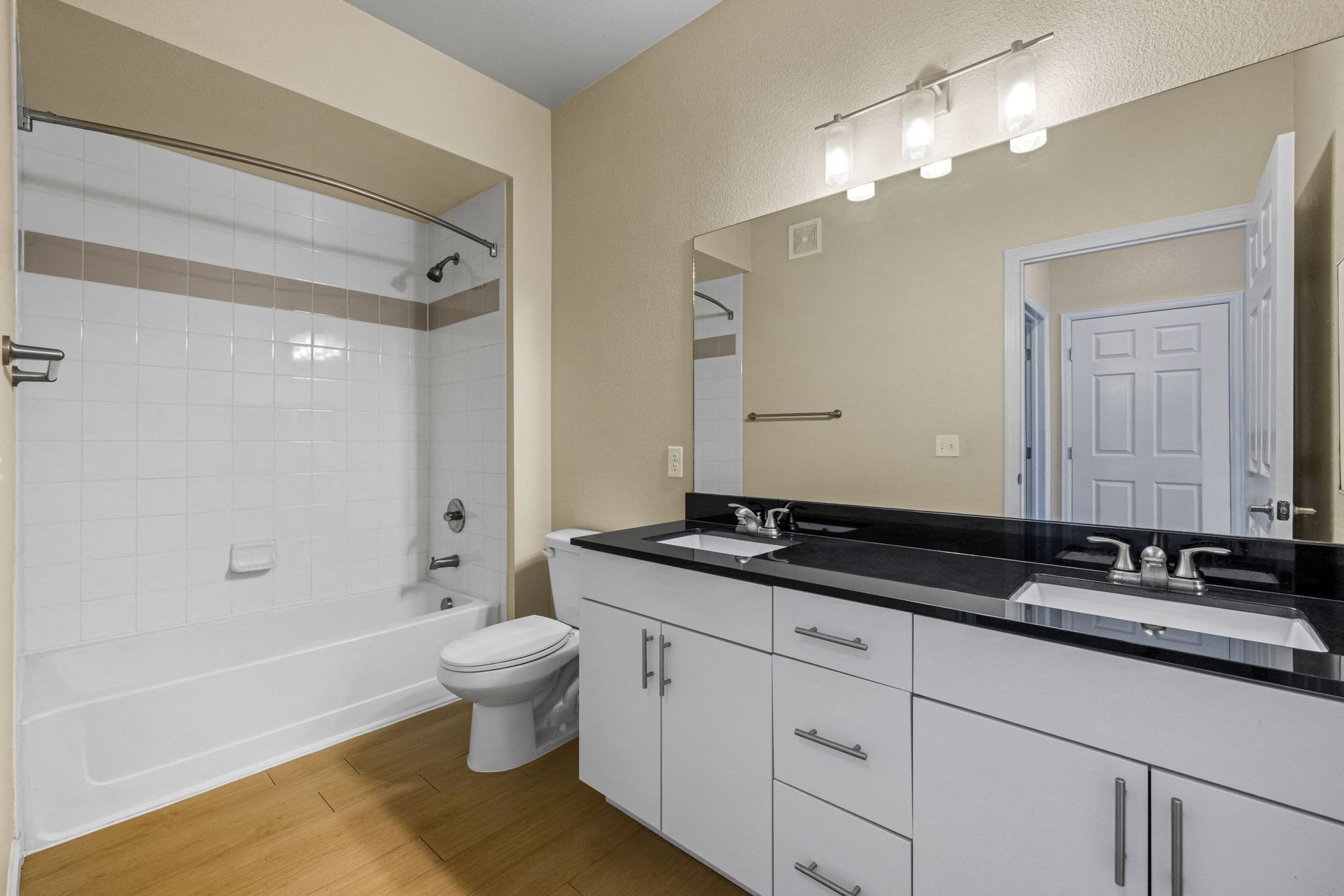 Bathroom with tub/shower, toilet, and double-sink vanity with a black countertop.
