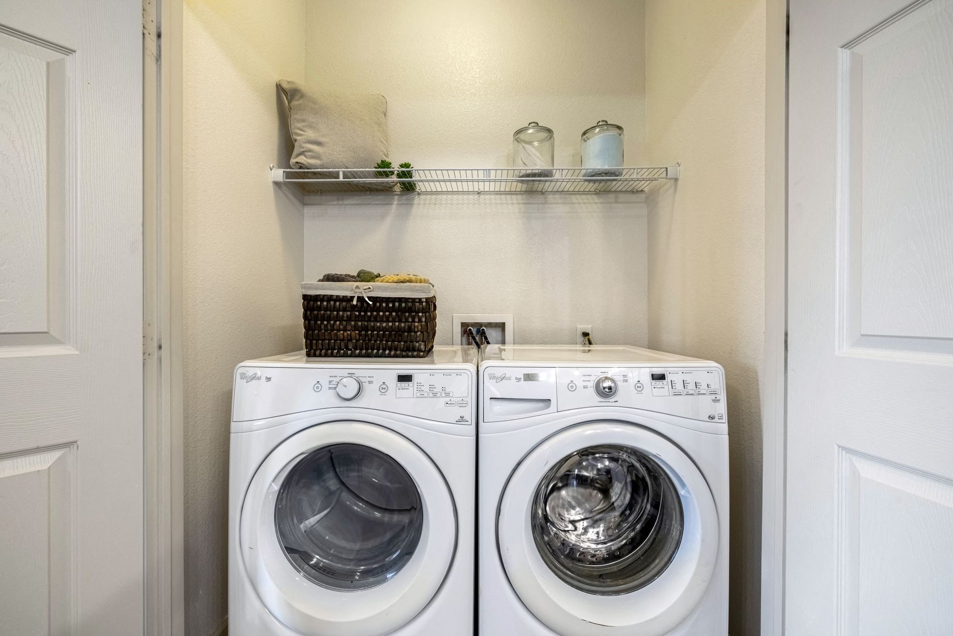 Front-loading washer and dryer side by side in a small laundry closet with a wire shelf above.