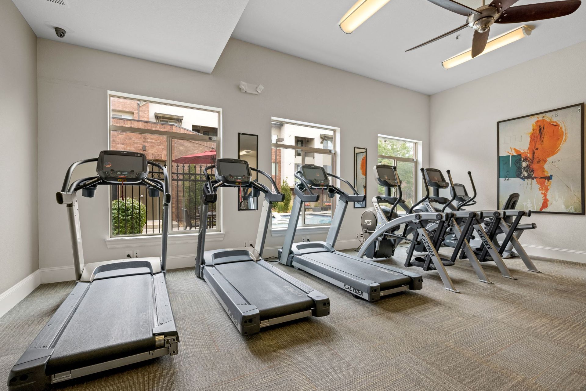 Fitness center with several treadmills and ellipticals by large windows.