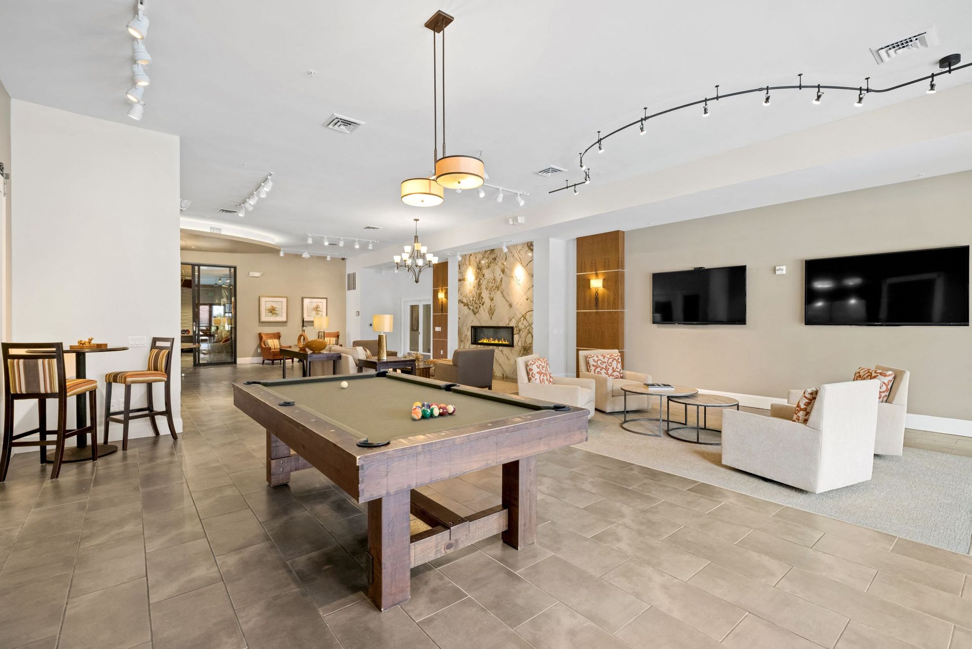 Spacious community lounge with a pool table, seating area, and wall-mounted TVs.
