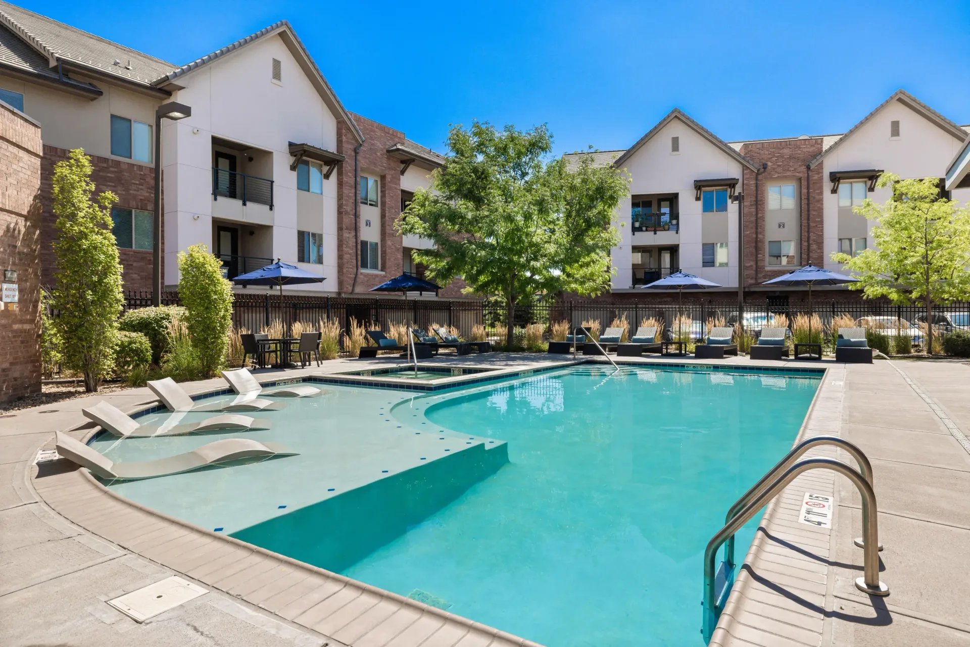Outdoor community pool with lounge chairs and umbrellas in a landscaped courtyard.