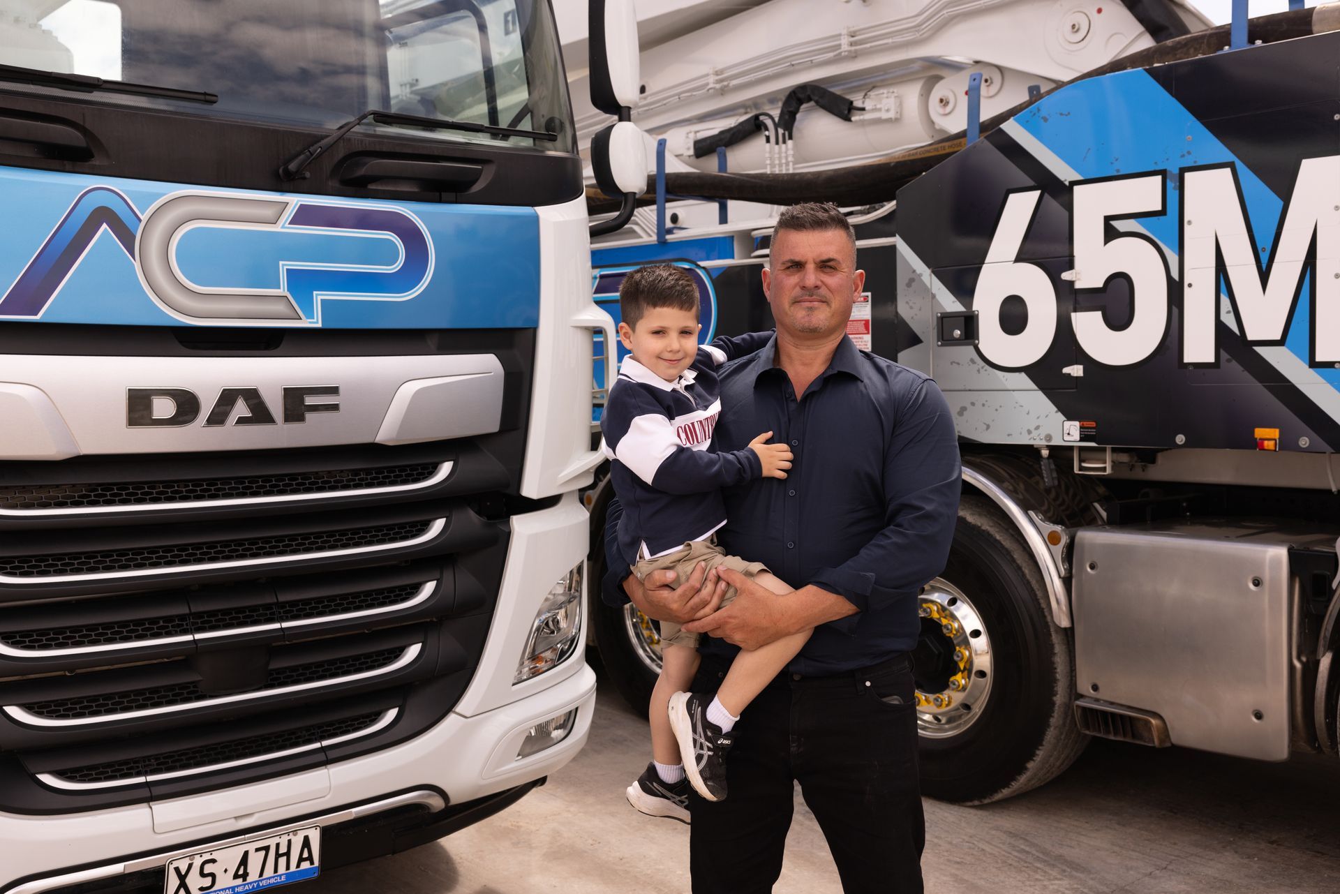 Man holding child in front of cement truck, logo 