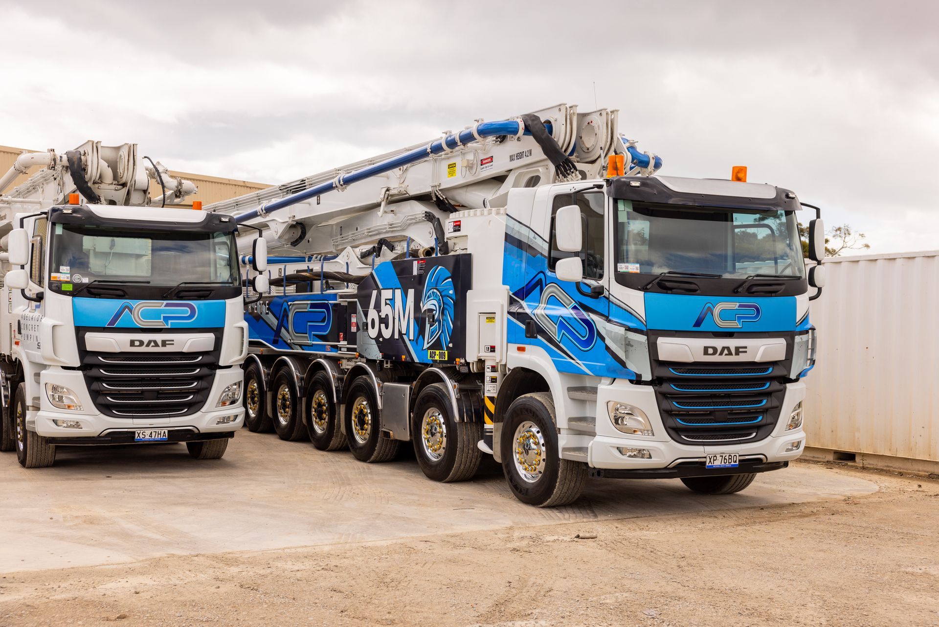 Two white and blue concrete pump trucks parked on gravel.