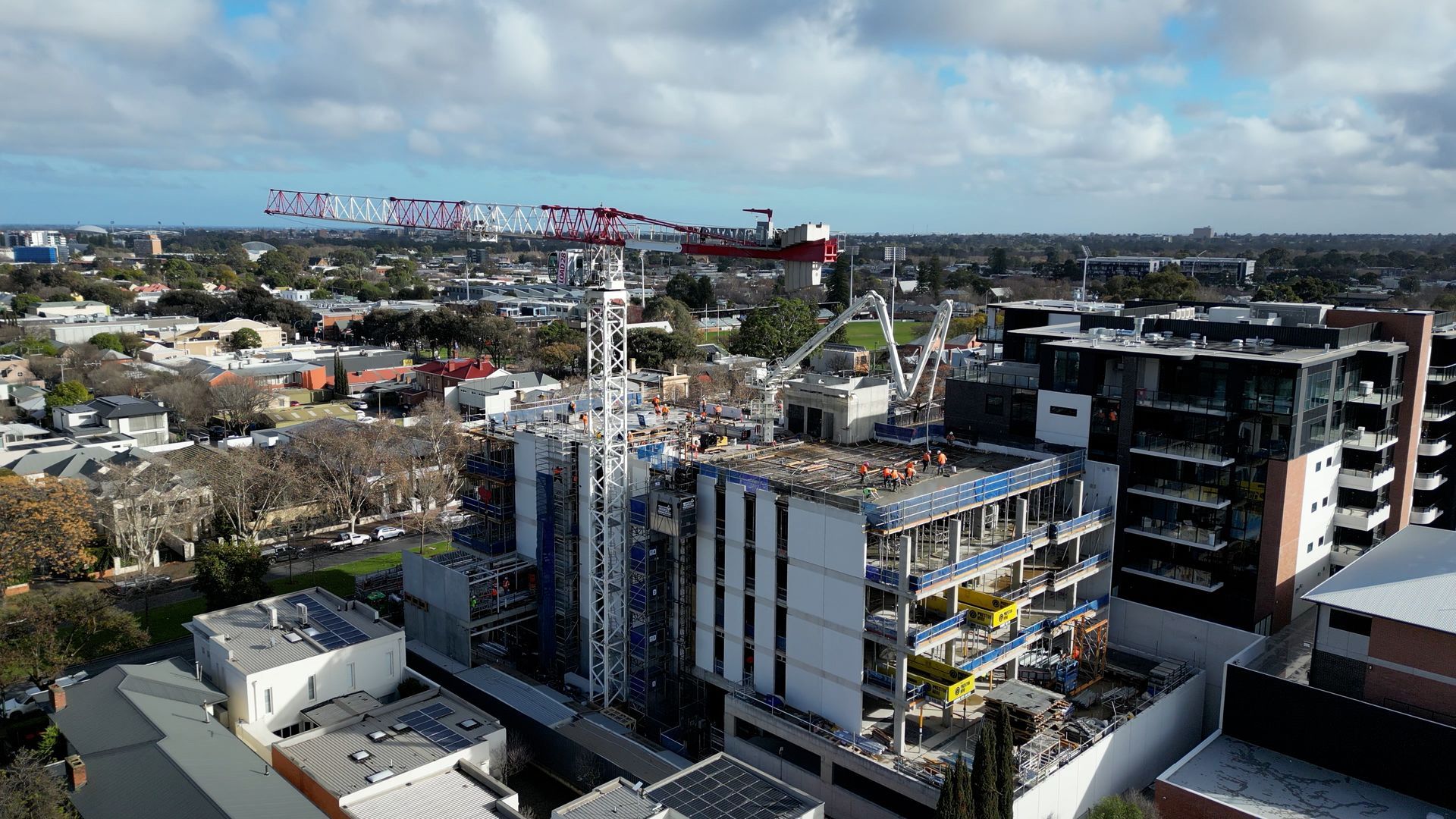 Construction site with tall cranes amidst buildings and cityscape under a blue sky.