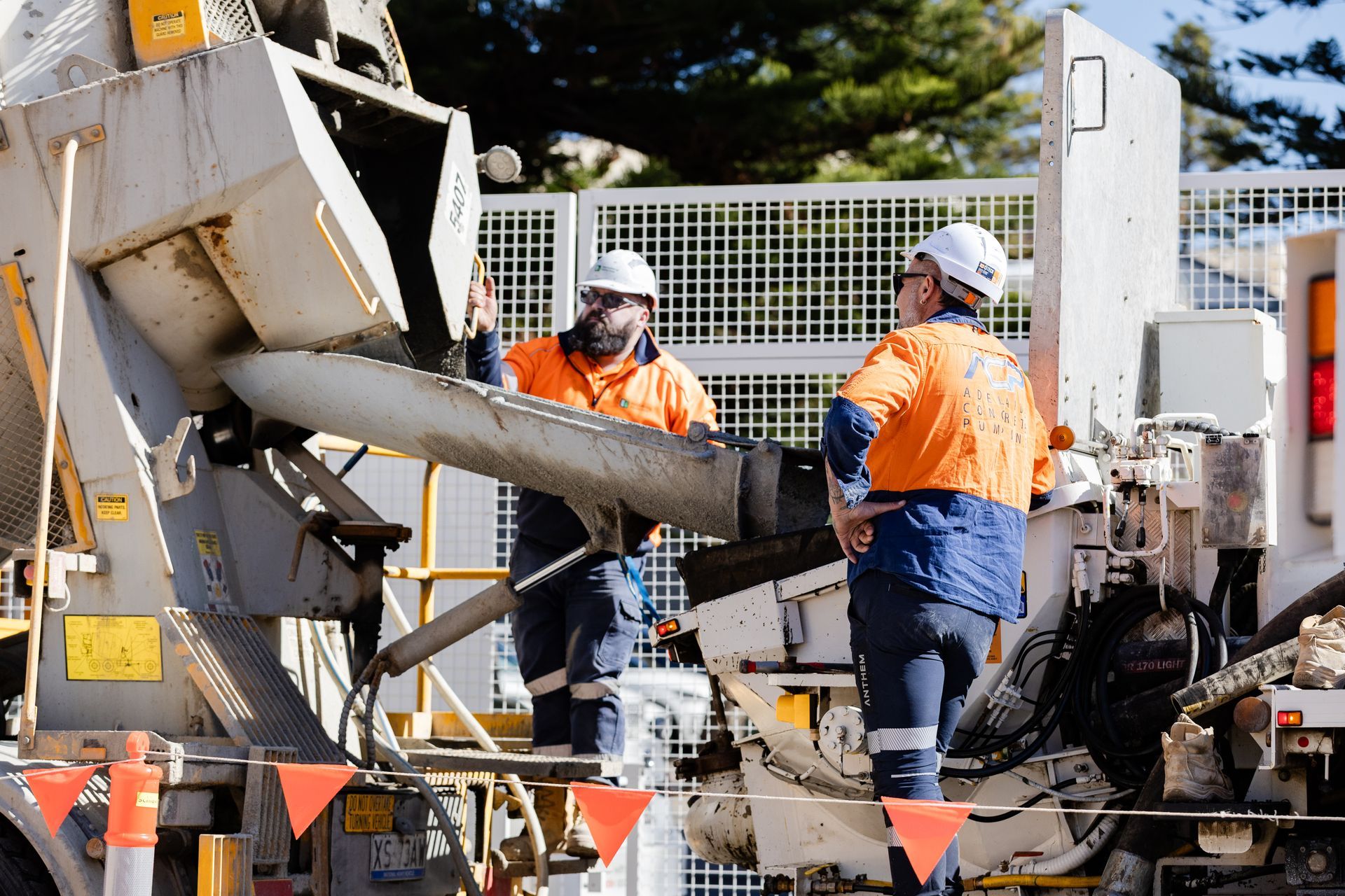 Man in yellow hard hat and coveralls, driving a truck, smiling at the camera.