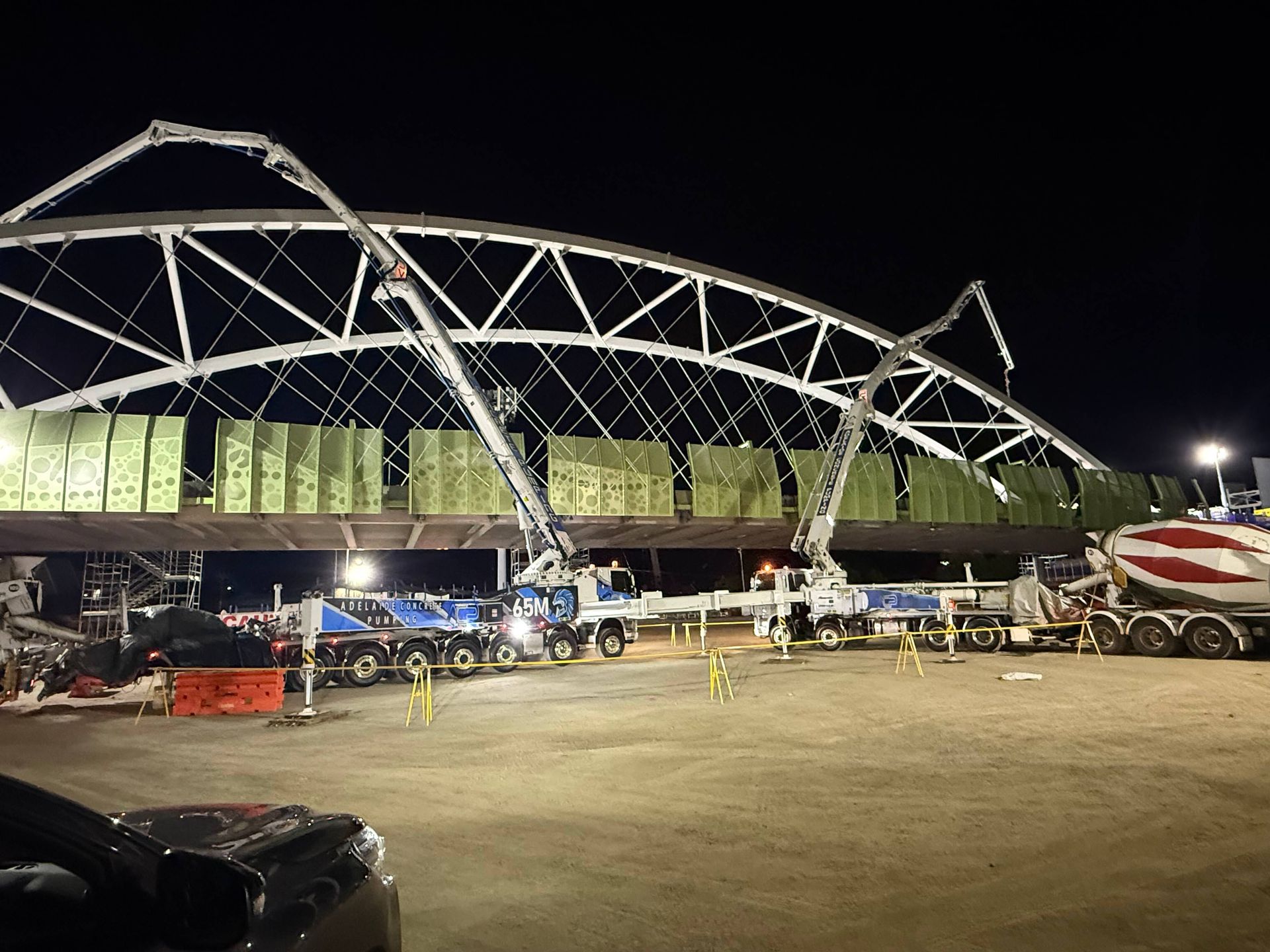 Nighttime construction: Concrete trucks pumping concrete into a bridge arch framework.
