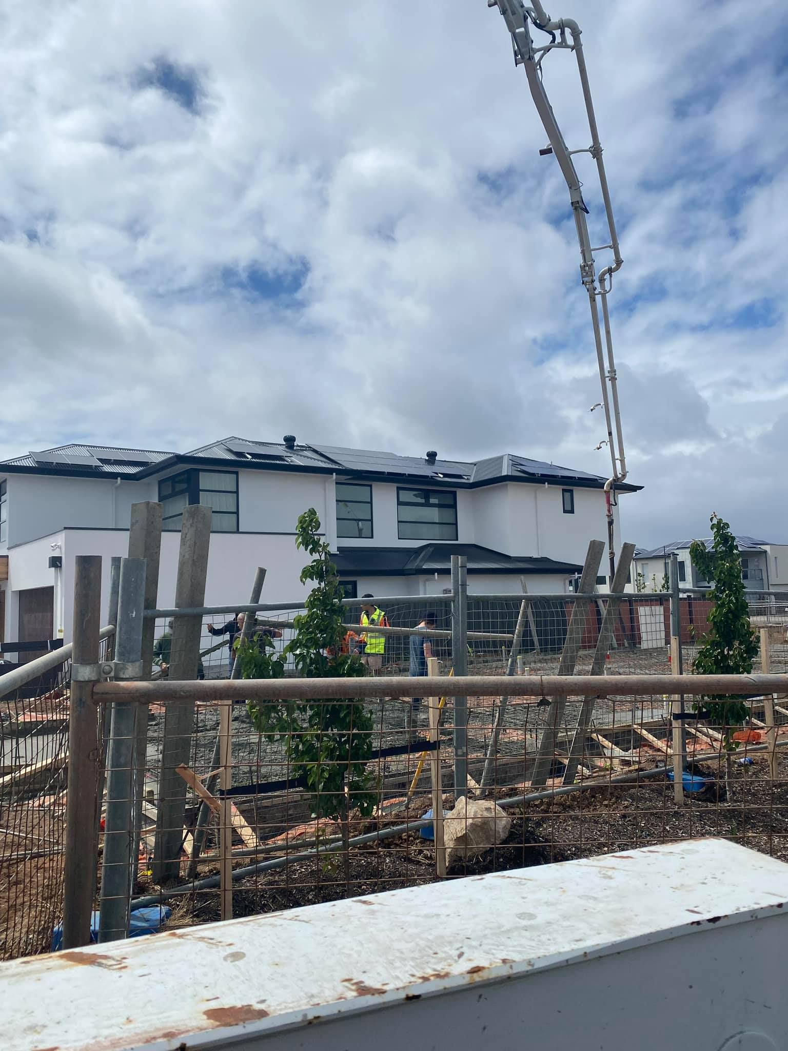 Construction site with concrete pump pouring, modern homes in background.