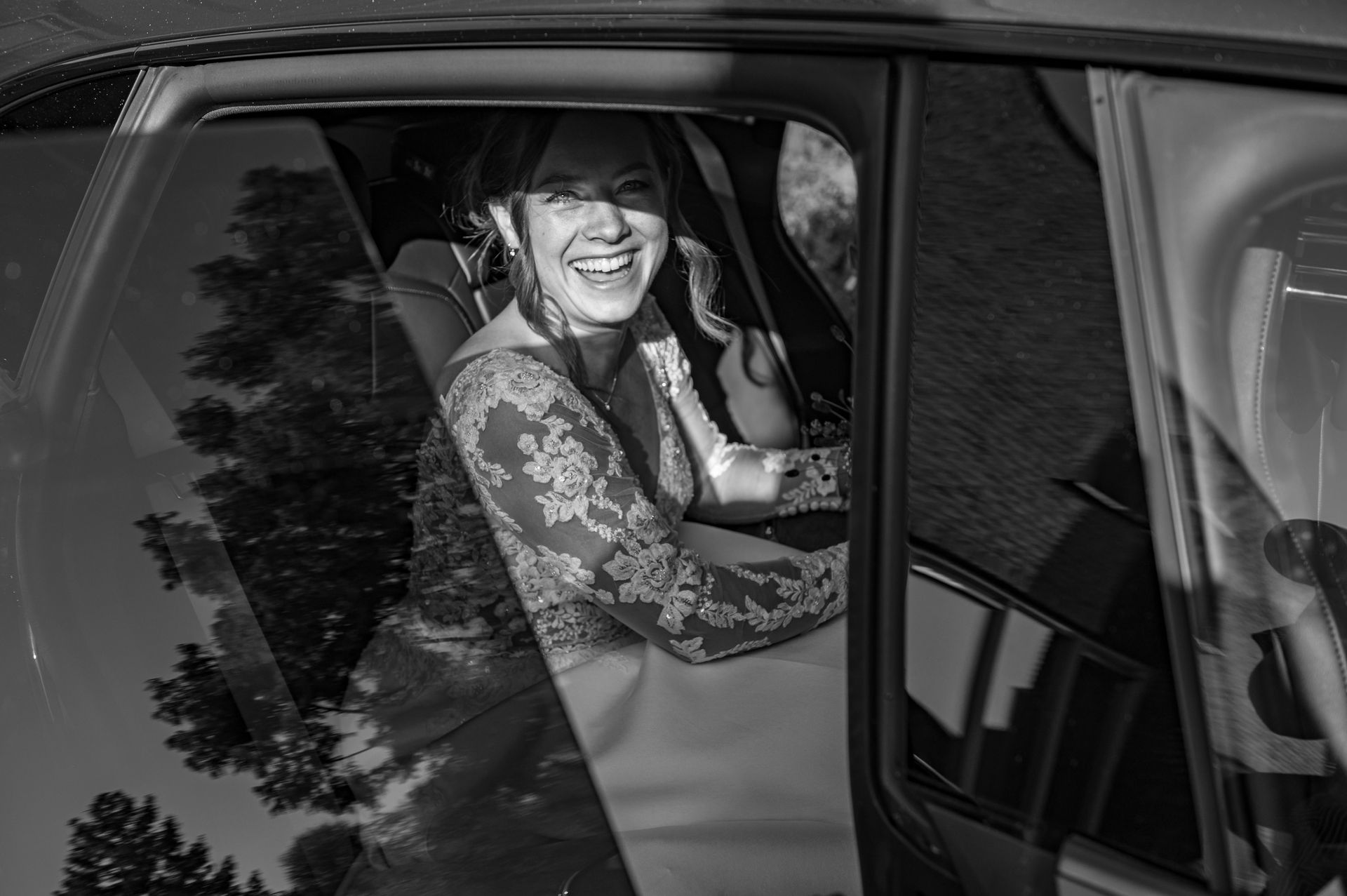 Een bruid zit op de achterbank van een auto en lacht.