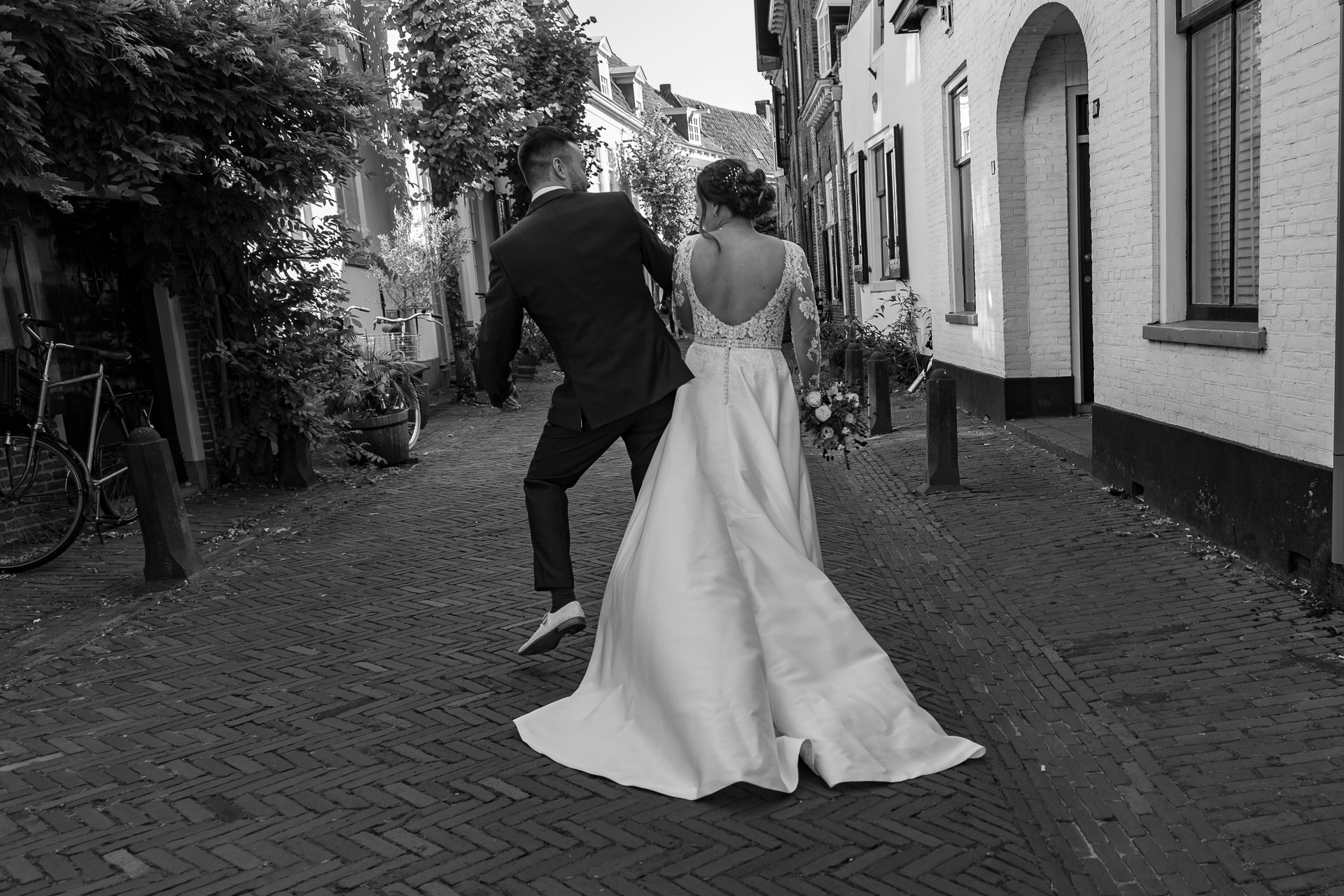 Een zwart-witfoto van een bruidspaar dat door een smalle straat loopt.