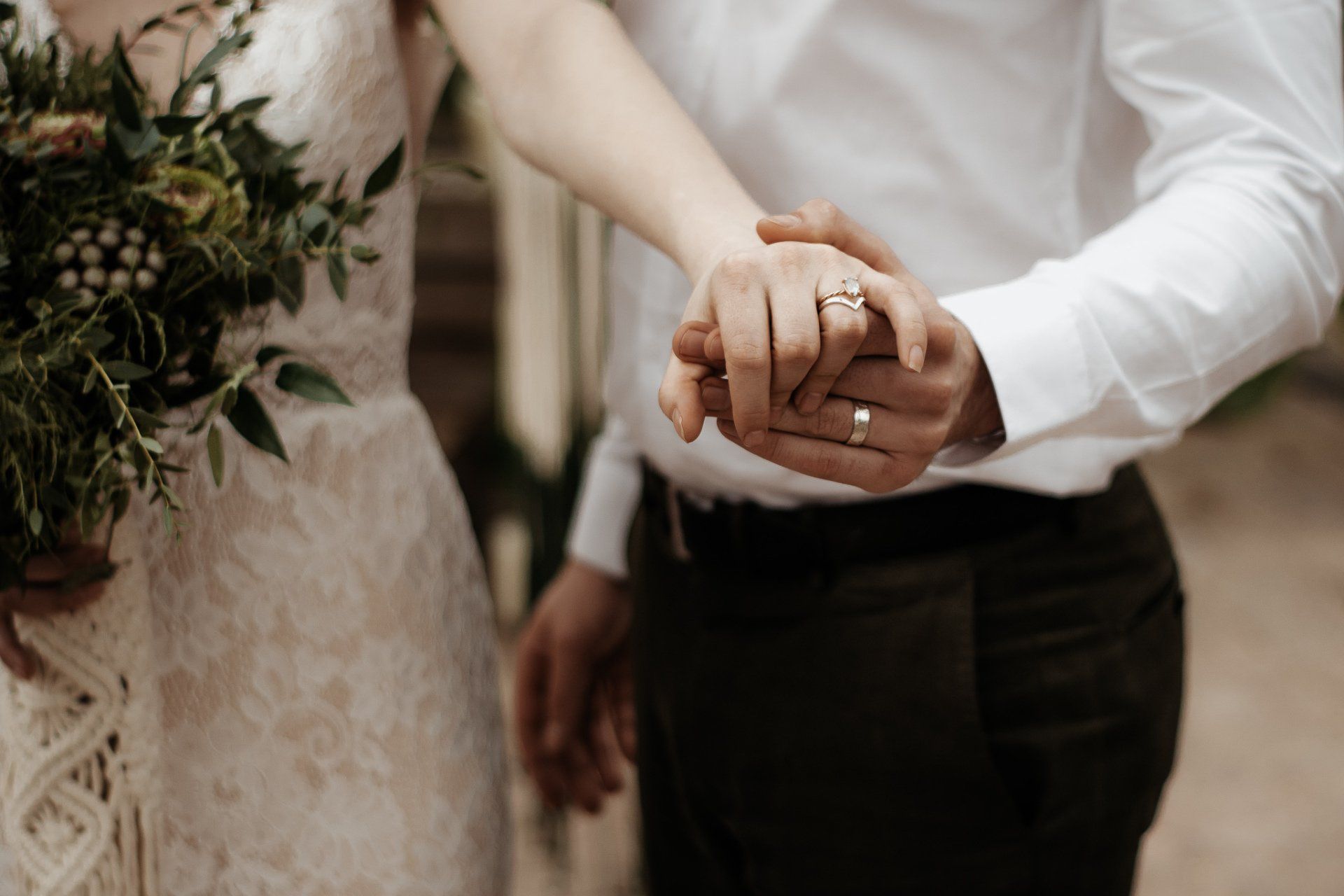 Een bruid en bruidegom houden elkaars handen vast en hebben hun trouwringen om.
