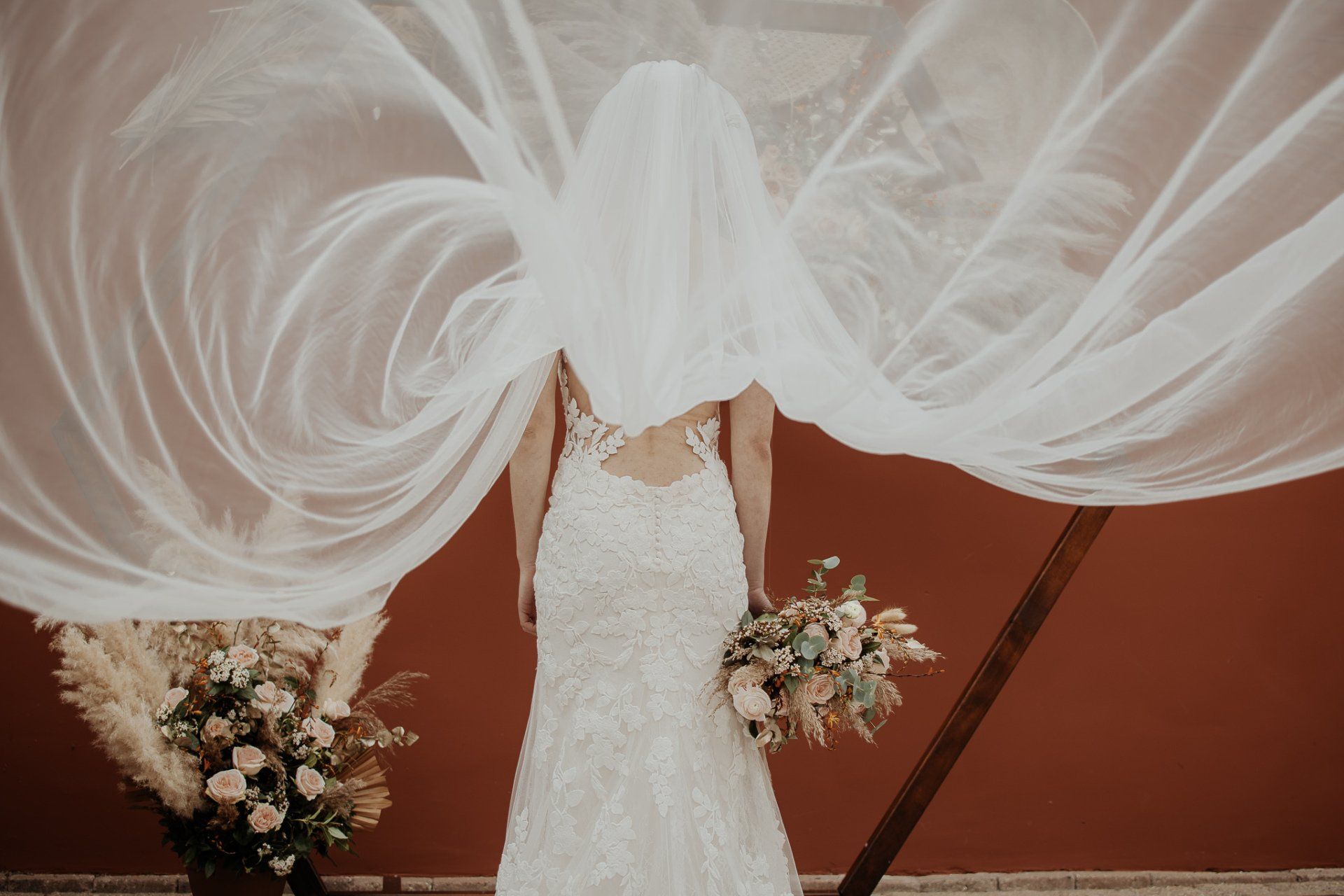 De bruid draagt een lange sluier en houdt een boeket bloemen vast.